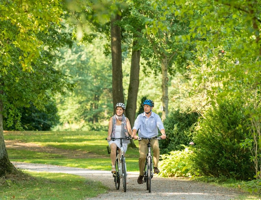 Zwei Radfahrer mit Helmen fahren auf dem Rheinradweg. Die Umgebung ist grün und friedlich, ideal für eine entspannte Fahrradtour