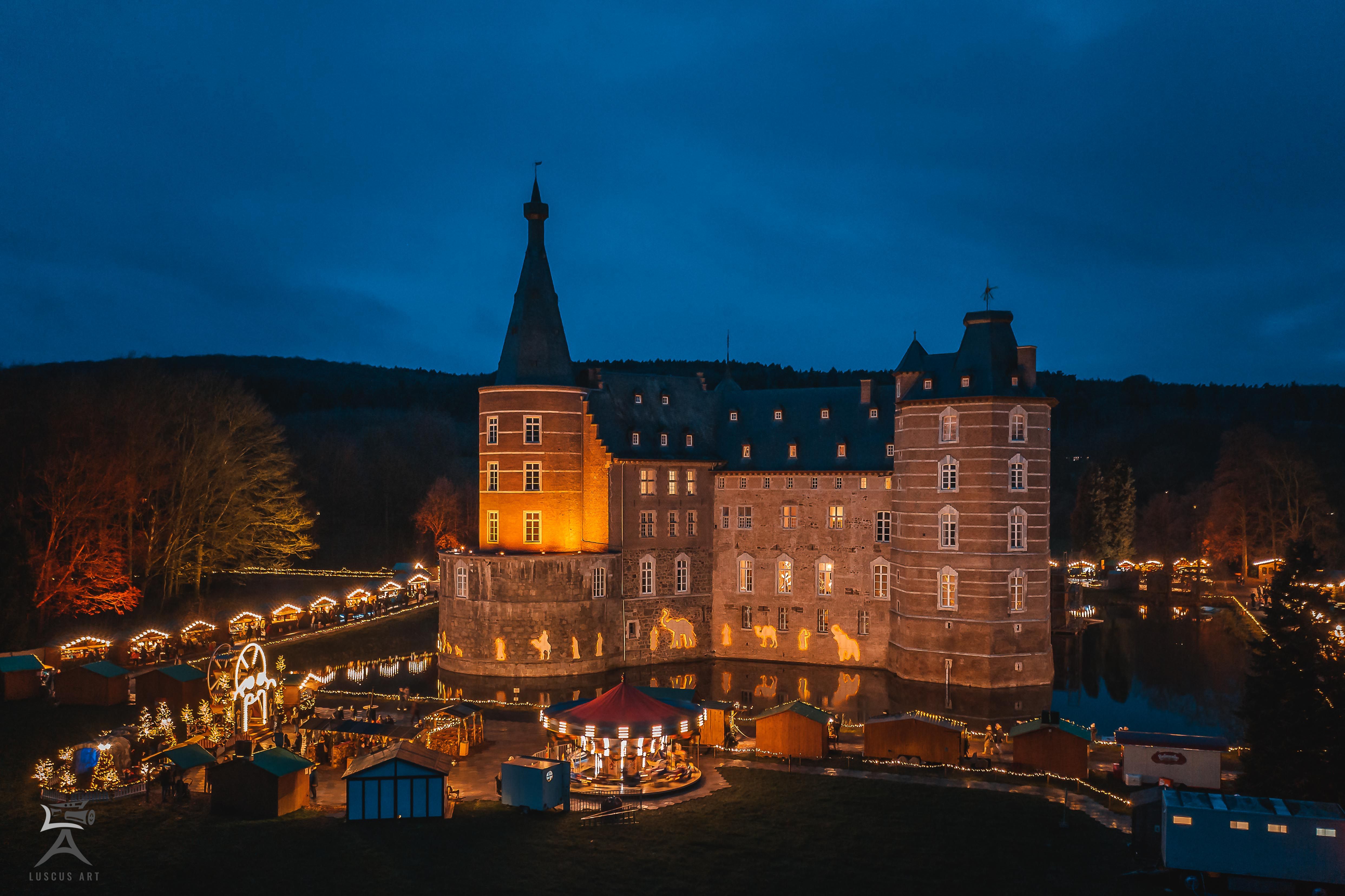 Schloss Merode bei Nacht, festlich beleuchtet mit Weihnachtsmarktständen im Vordergrund.