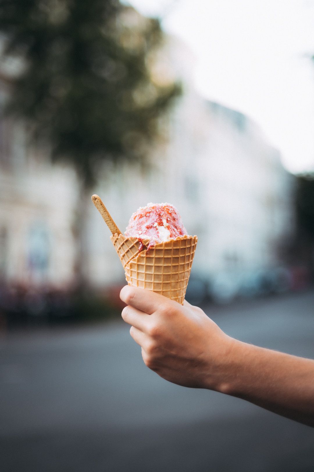 Hand hält Eiswaffel mit Vanilleeis und Erdbeersauce
