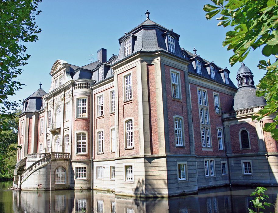 Schloss mit rotem Backstein und grauem Dach, umgeben von Wassergraben. Das Schloss Ostbevern ist am fünften Reisetag eines der Ziele am Wegesrand.