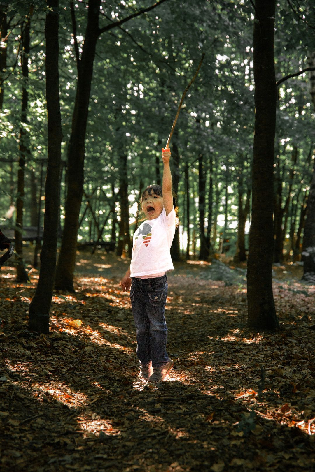 Sommerlich gekleidetes Mädchen im Wald hält einen Ast hoch