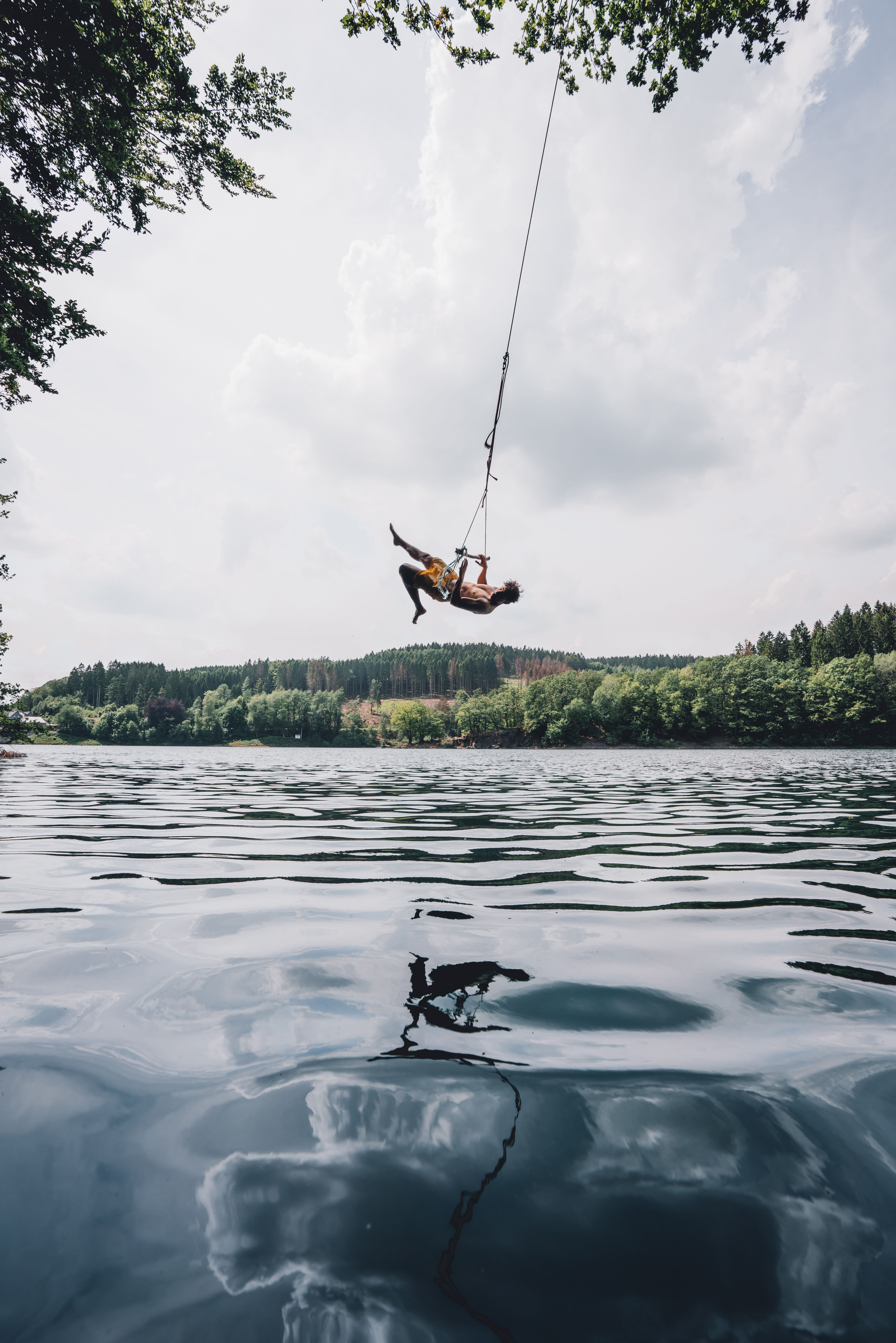 Person schwingt an einer Schaukel über dem Wasser der Aggertalsperre mit bewaldetem Ufer im Hintergrund.