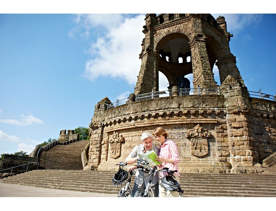 Zwei Personen mit E-Bikes vor dem Kaiser-Wilhelm-Denkmal und betrachten eine Karte.