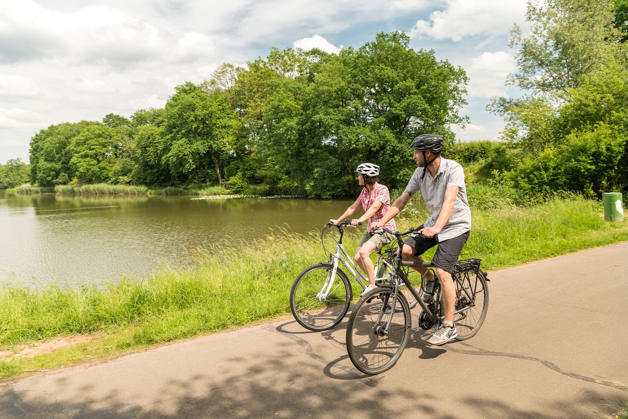 Zwei Radfahrer auf dem Maare-Mosel-Radweg entlang eines Sees mit Bäumen im Hintergrund.