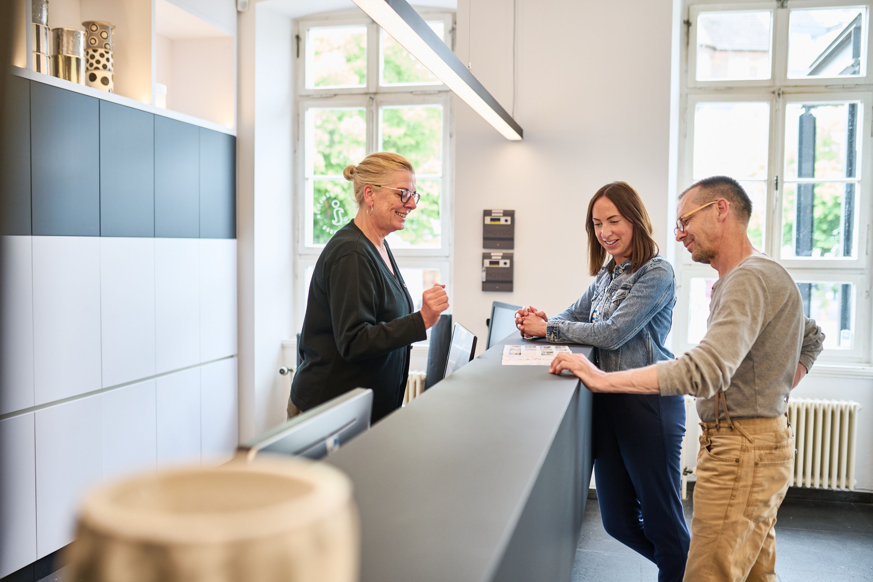 Drei Personen sprechen freundlich mit einer Mitarbeiterin an der Rezeption der Tourist Information Siegburg.