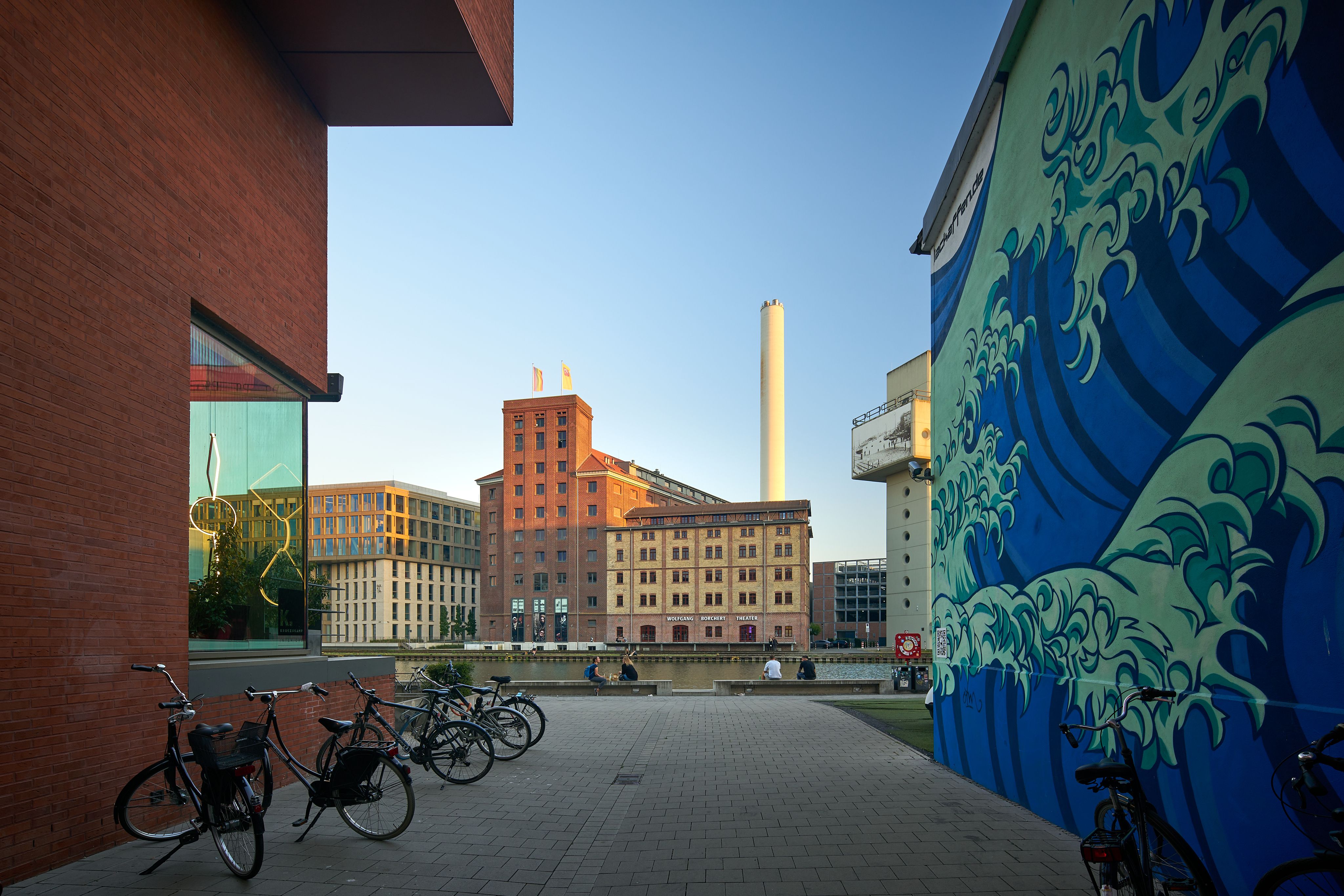 Blick auf den Hafen Münster mit modernen Gebäuden, einem Wandgemälde und Fahrrädern im Vordergrund.