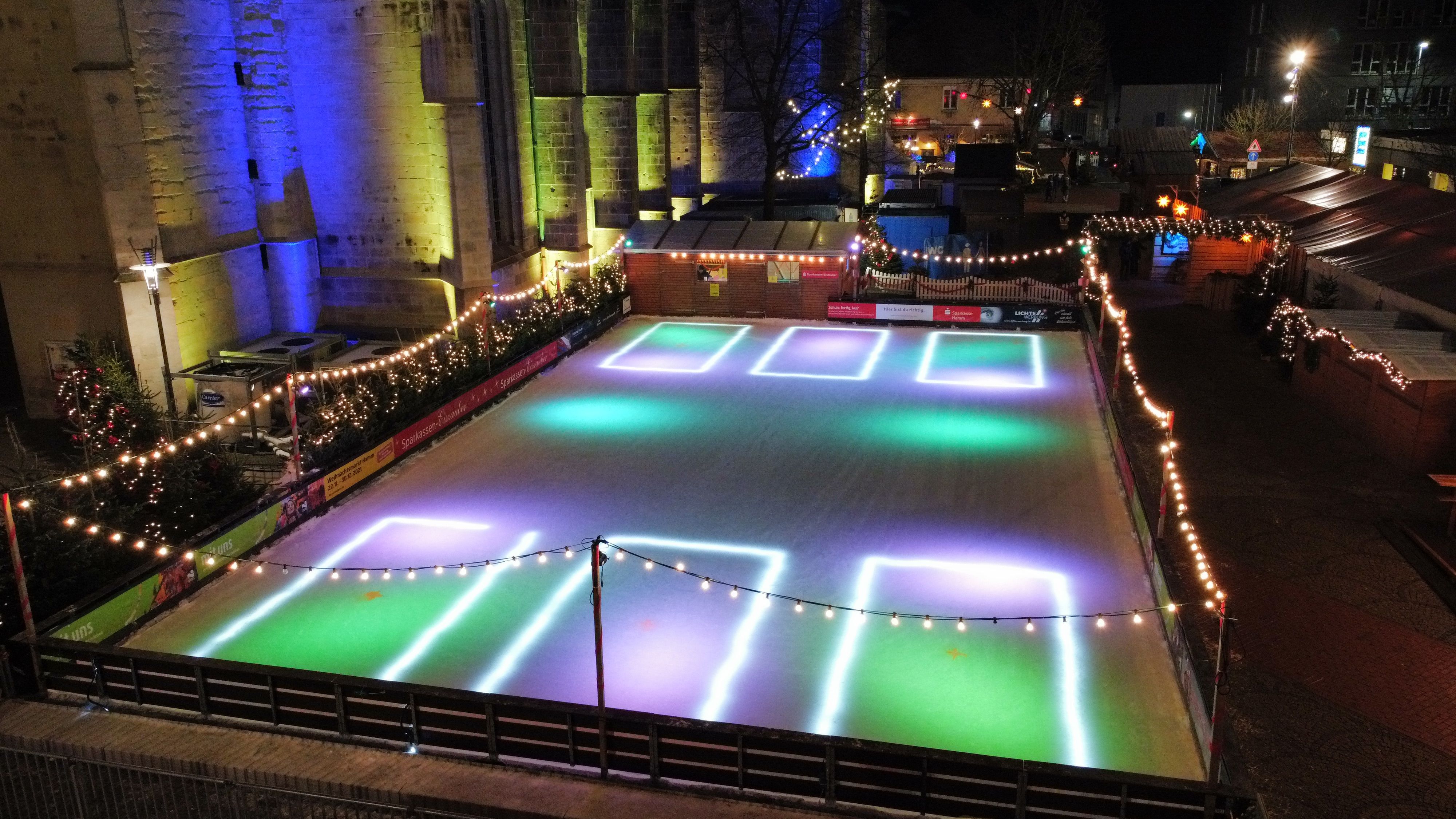 Eine beleuchtete Eisbahn auf dem Weihnachtsmarkt in Hamm, umgeben von Lichterketten und Tannenbäumen.