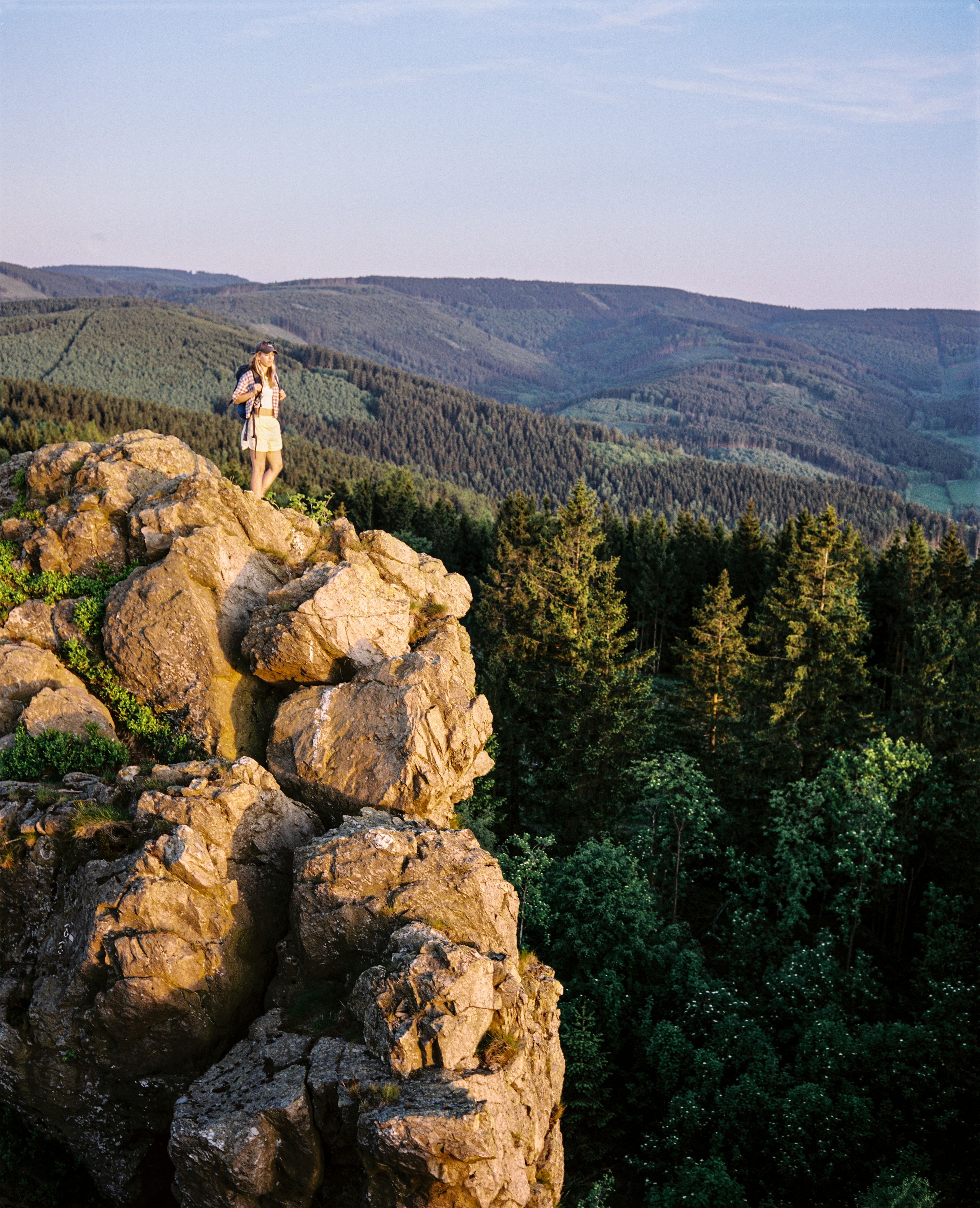 Frau mit Wanderrucksack steht auf Bruchhauser Steinen beim Rothaarsteig umgeben von dichtem Wald.