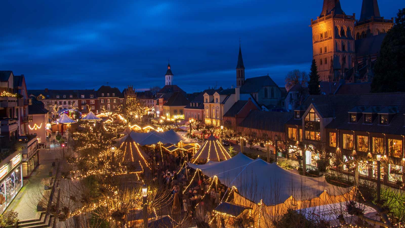 Der Weihnachtsmarkt in Xanten erstrahlt bei Nacht in festlichem Lichterglanz mit zahlreichen Ständen und Zelten.