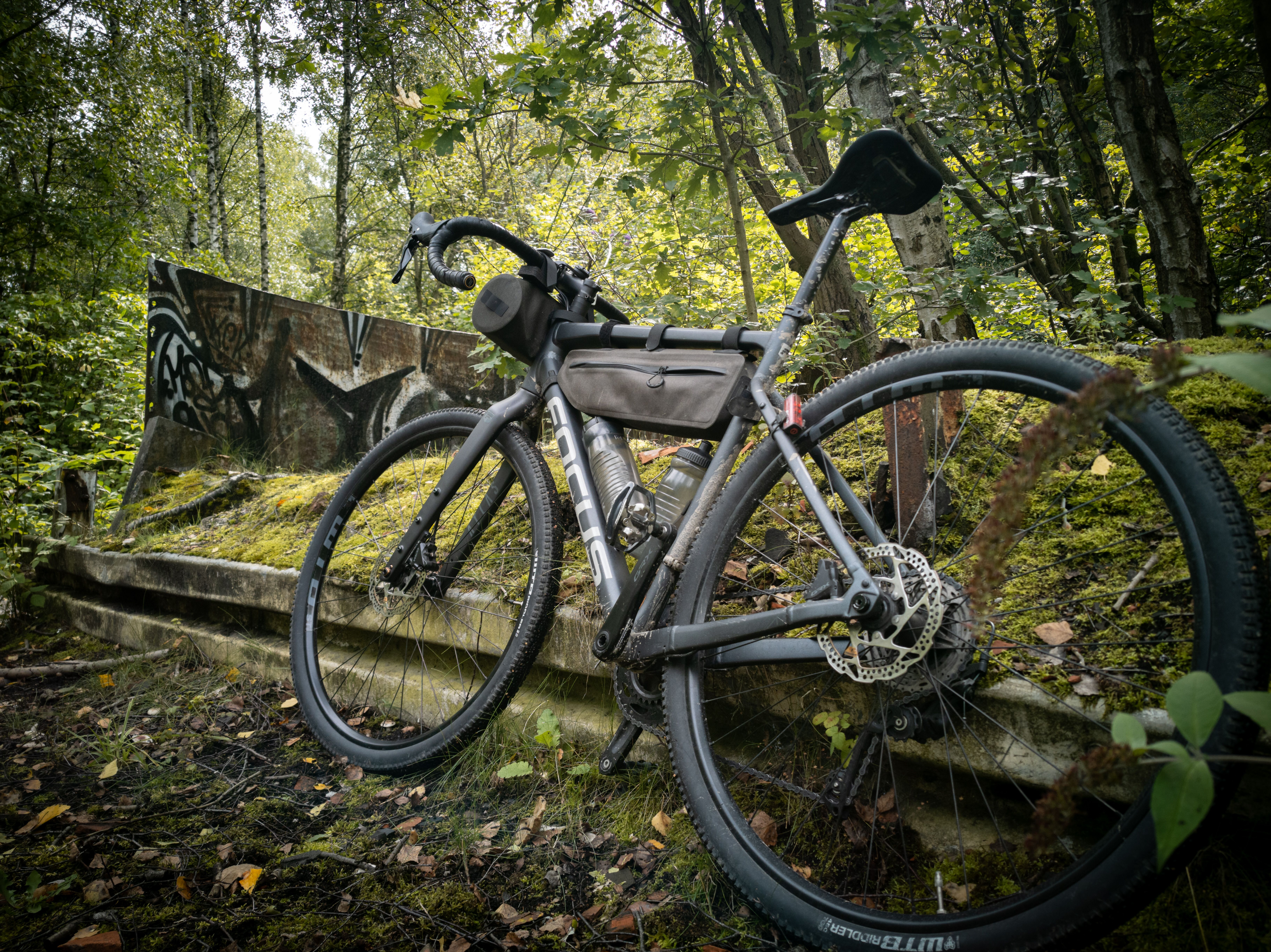 Ein Gravelbike lehnt an einer mit Graffiti bedeckten Betonwand im Wald.