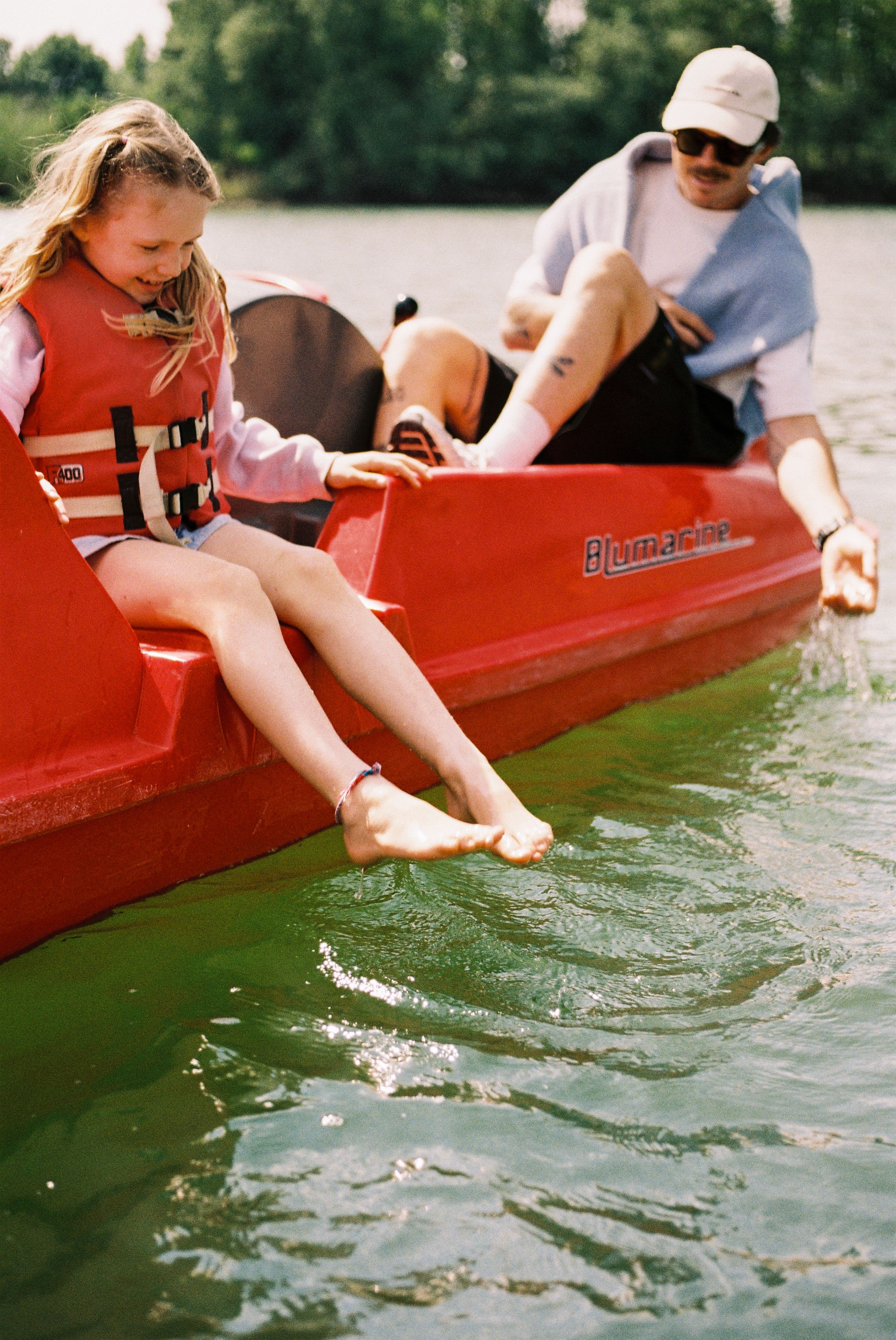 Ein Kind und ein Erwachsener sitzen in einem roten Tretboot auf der Xantener Südsee. Das Kind trägt eine Schwimmweste und hält die Füße ins Wasser.