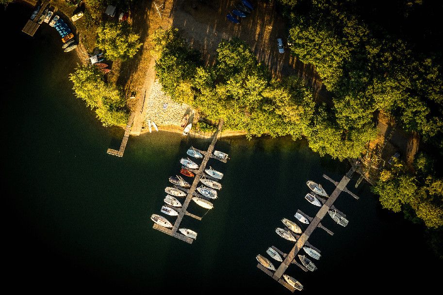 Luftaufnahme des Haddorfer Sees mit Bootsstegen und Booten, umgeben von dichtem Wald und einem kleinen Strandbereich.