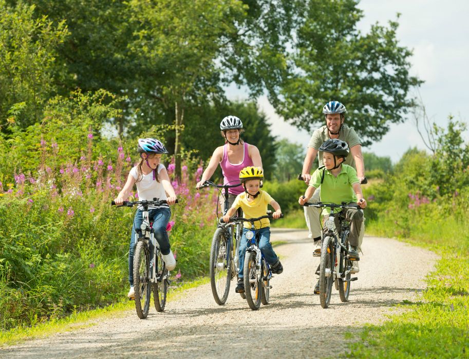Familie fährt auf einem Schotterweg mit Fahrrädern durch eine grüne Landschaft.