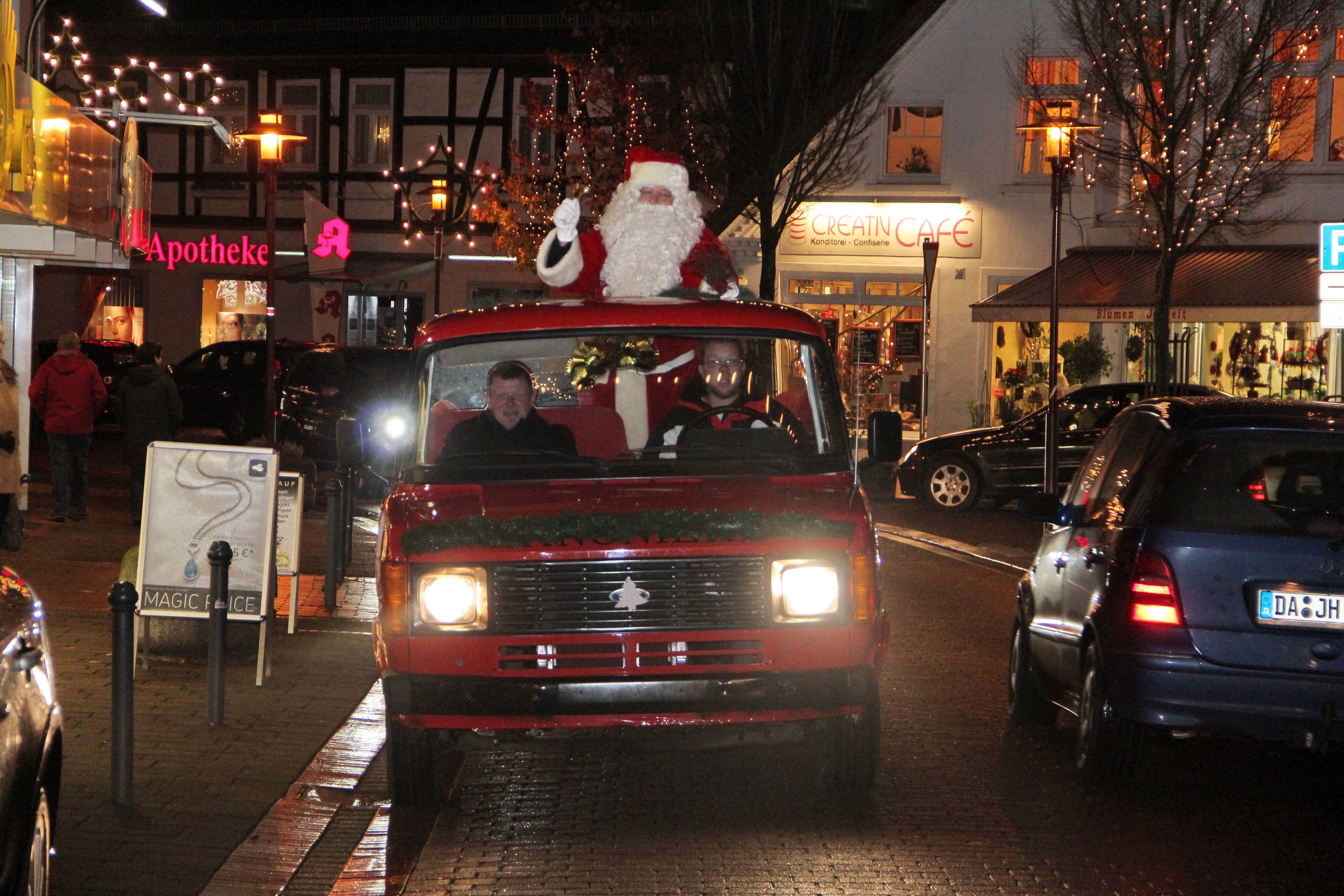 Ein Weihnachtsmann steht auf einem roten Fahrzeug in einer festlich beleuchteten Straße in Rahden.