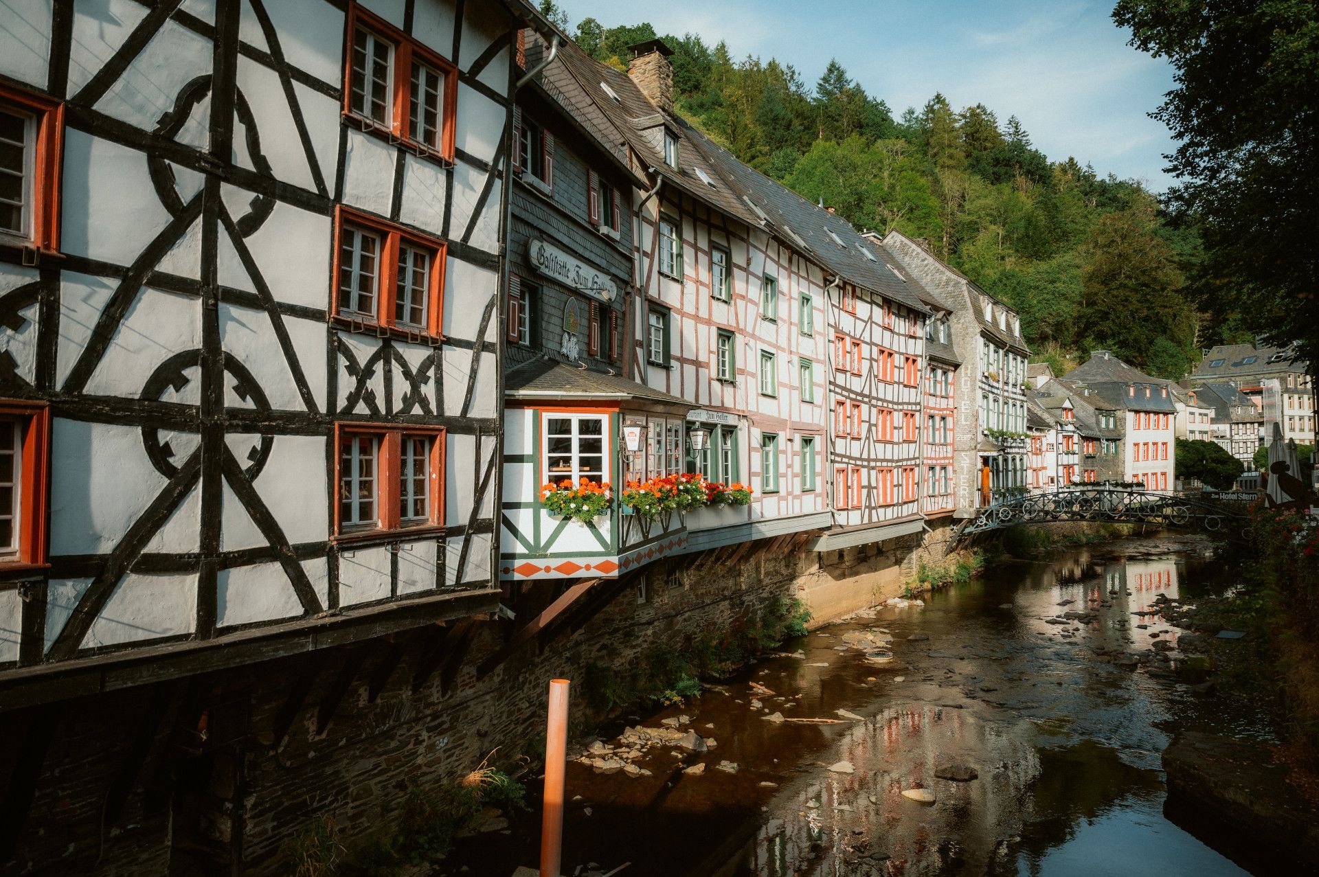 Fachwerkhäuser in Monschau entlang eines Flusses mit Brücke.