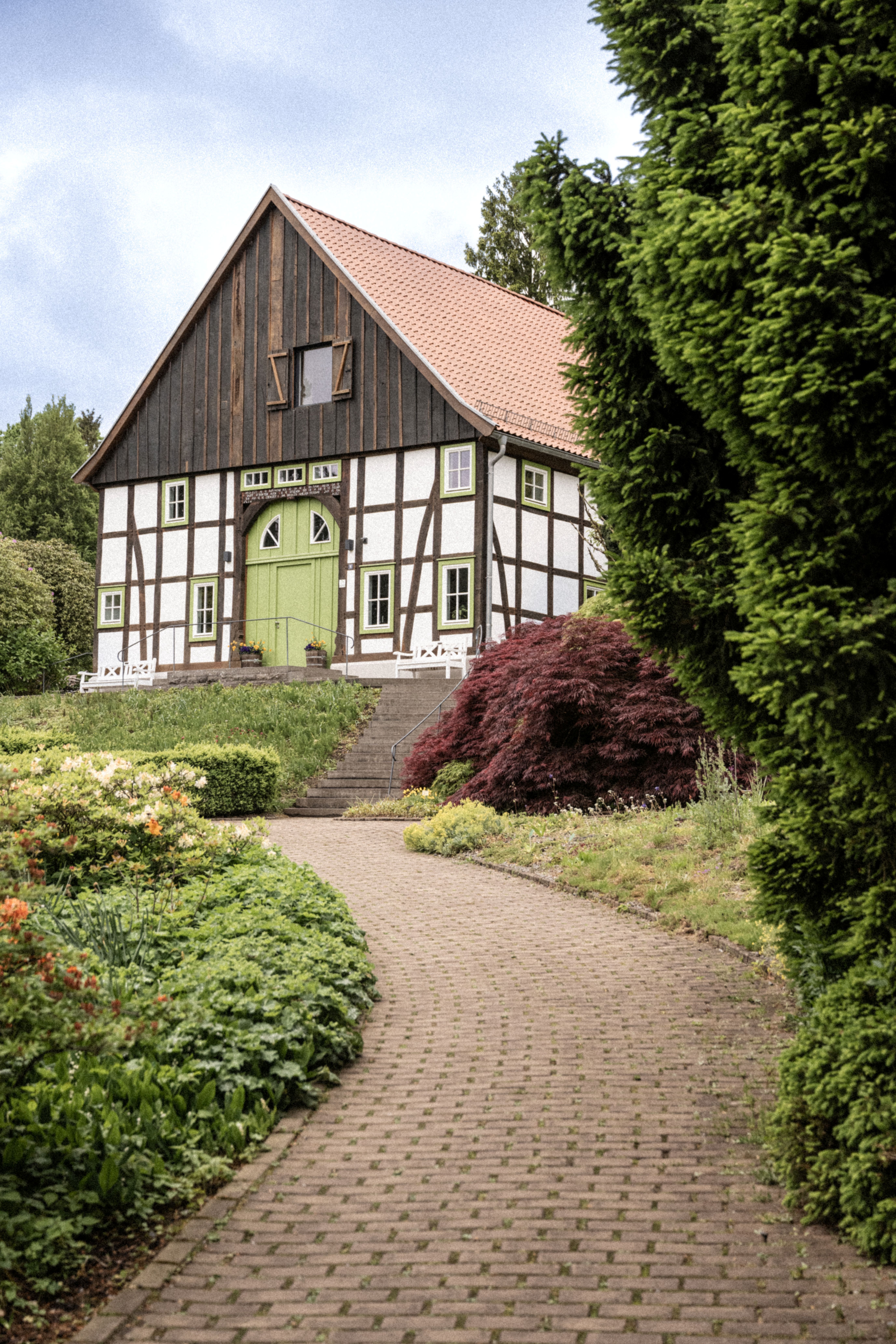 Ein charmantes Fachwerkhaus im Botanischen Garten Bielefeld, umgeben von grünen Pflanzen und einem gepflasterten Weg, der zum Eingang führt.