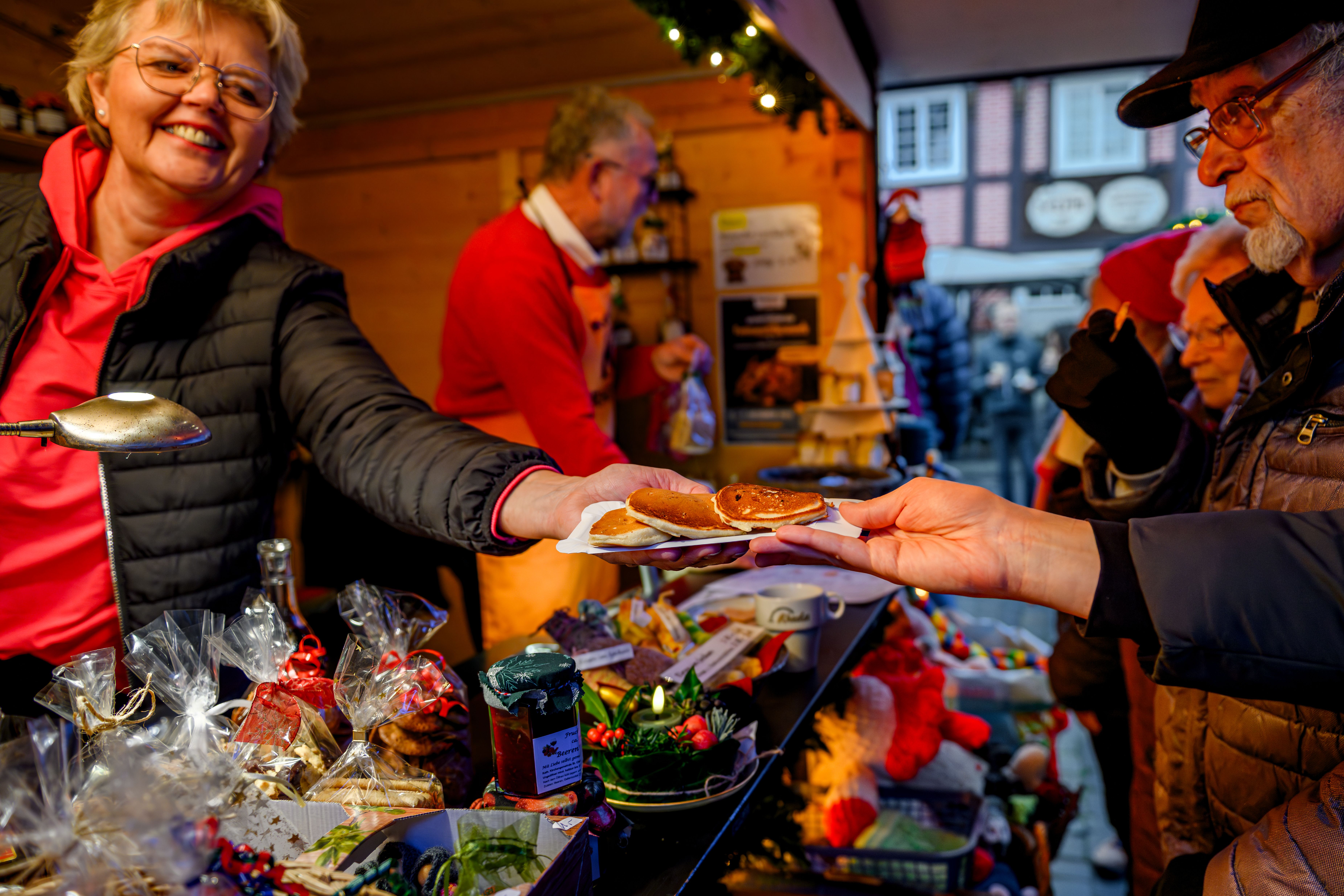 Verkäuferin übergibt einem Kunden auf dem Weihnachtsmarkt in Rheda Pfannkuchen.