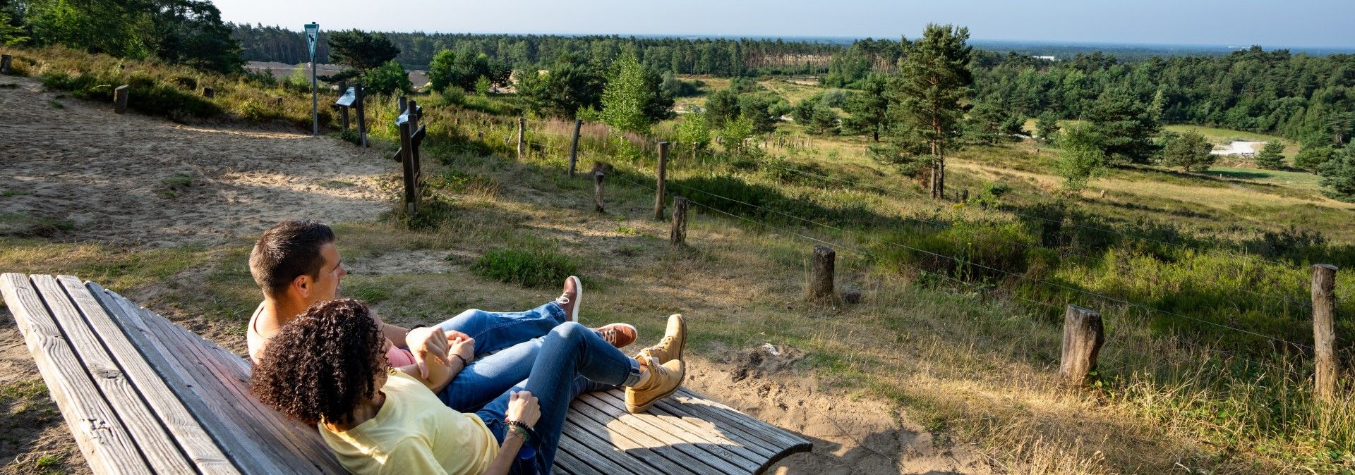 Zwei Personen sitzen auf einer Bank und genießen den Ausblick auf die grüne Landschaft der Senne bei Oerlinghausen.
