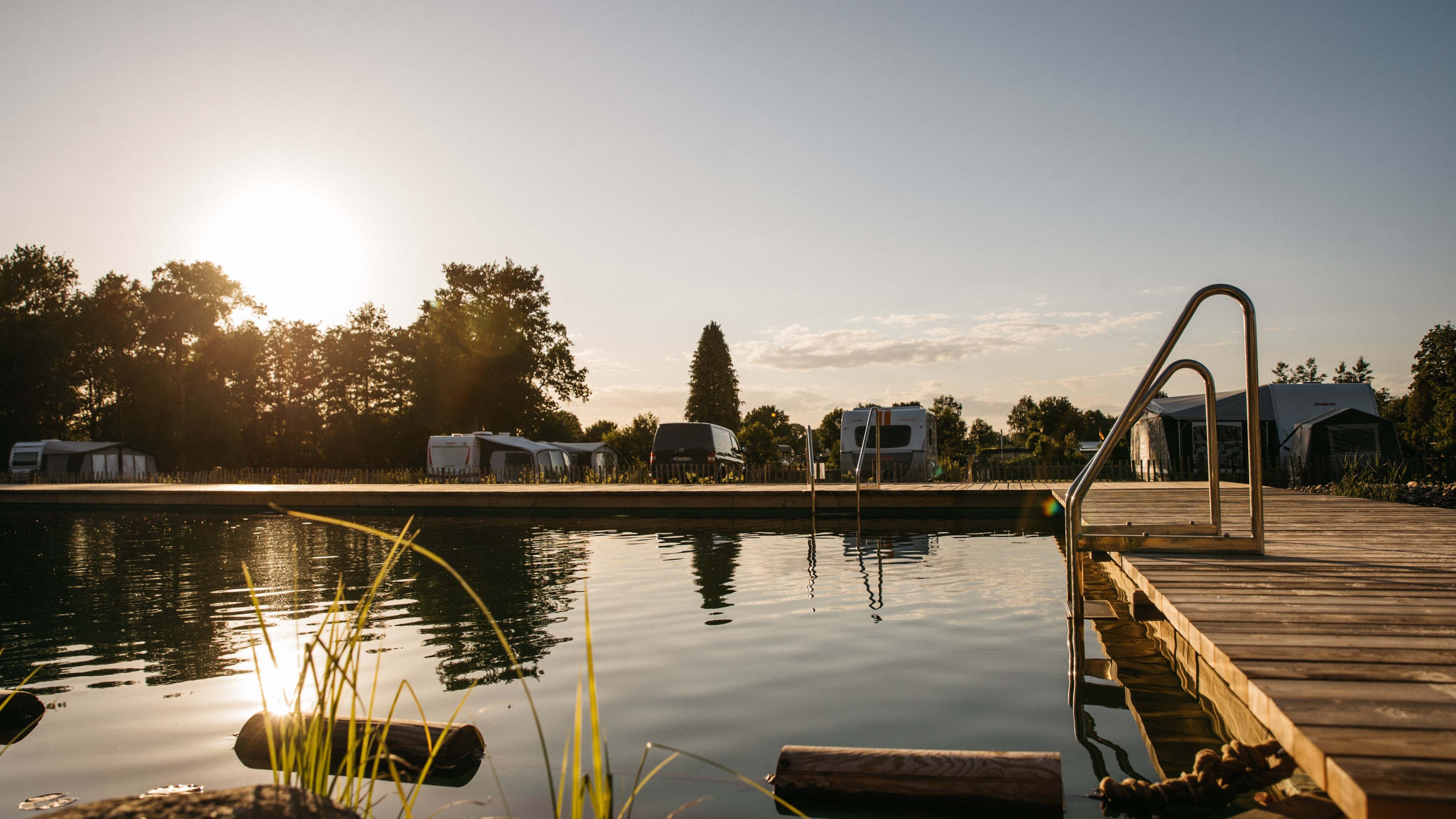 Pool im Abendlicht mit Wald und Caravans im Hintergrund 