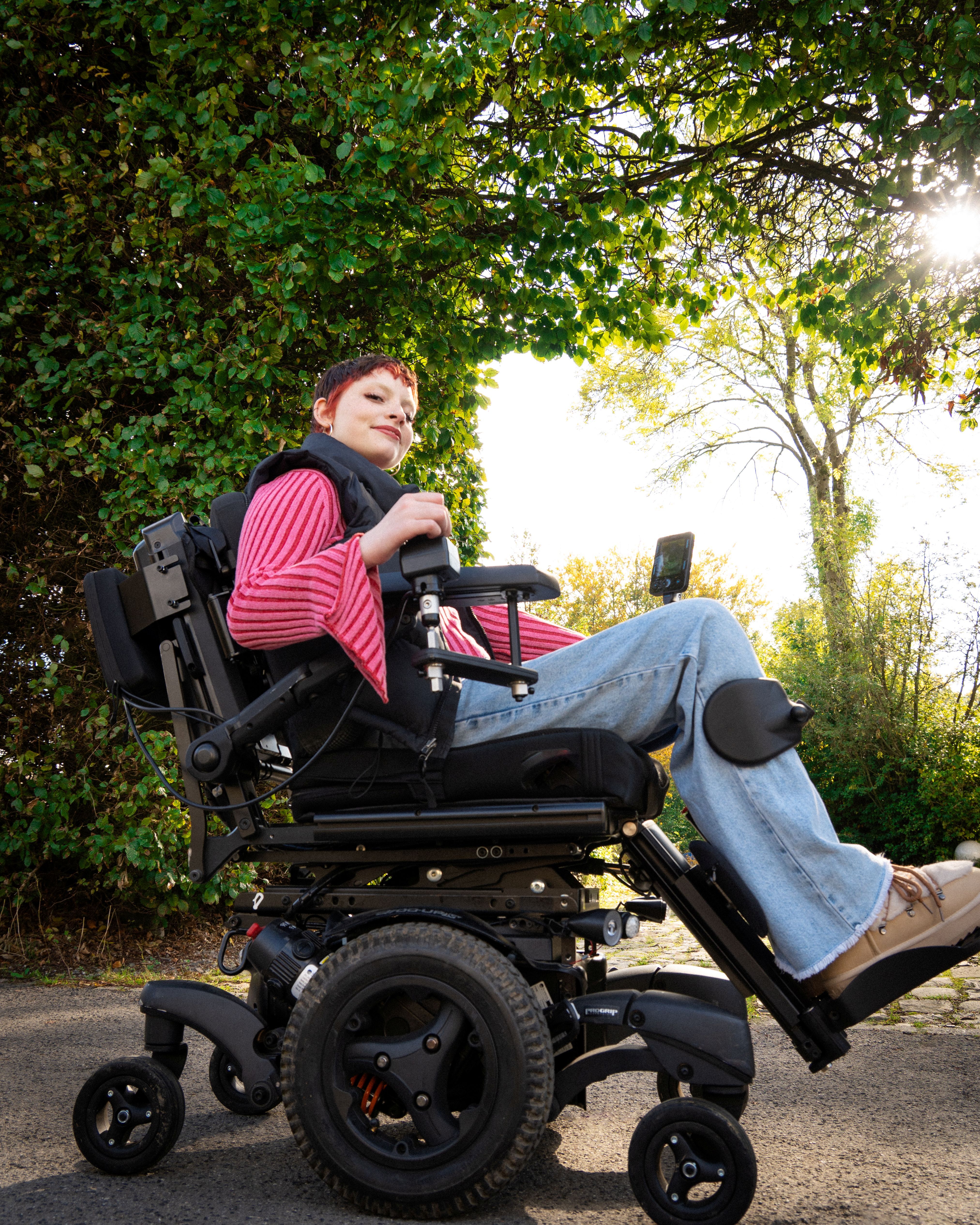 Rollstuhlfahrerin befindet sich vor einer Hecke im Sonnenschein