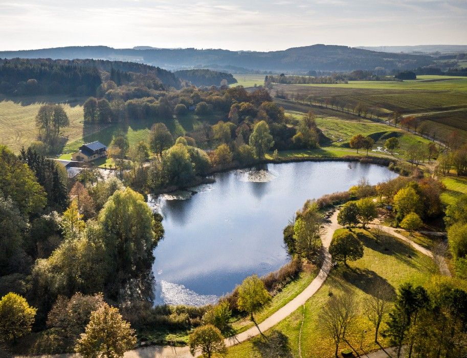 Luftaufnahme eines Sees im Bolsdorfer Tälchen, umgeben von Wäldern und Feldern.