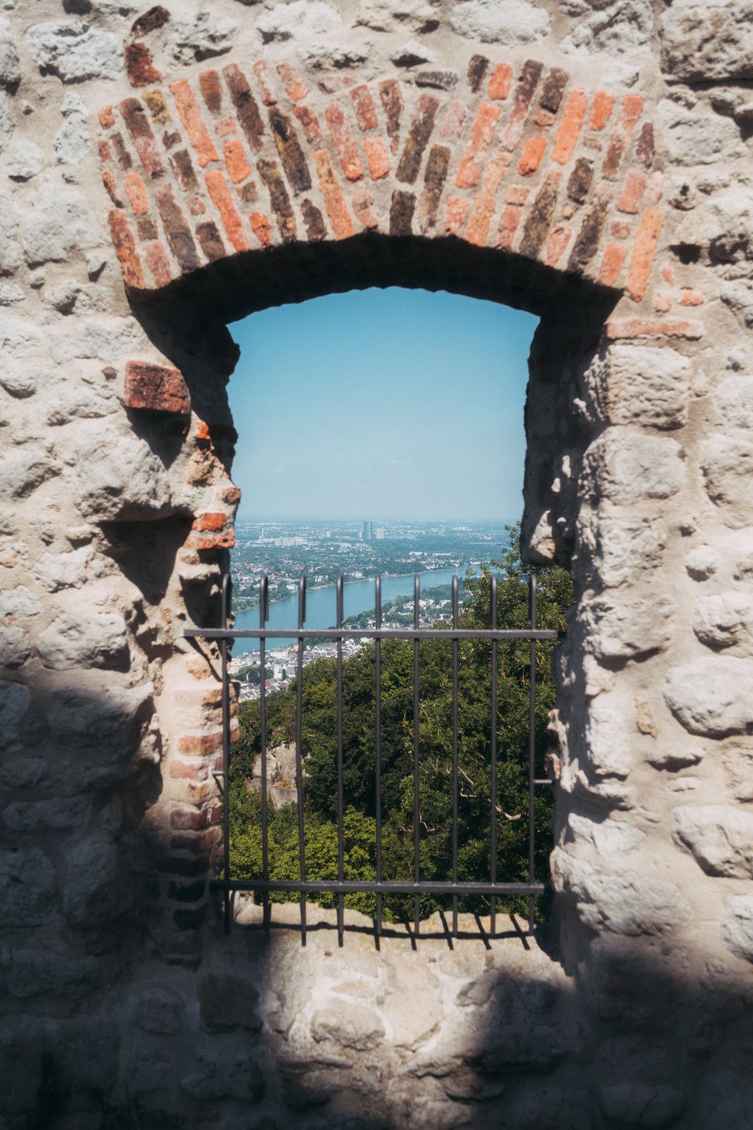 Blick durch ein altes Steinfenster mit Gitter auf den Rhein und die umliegende Landschaft.
