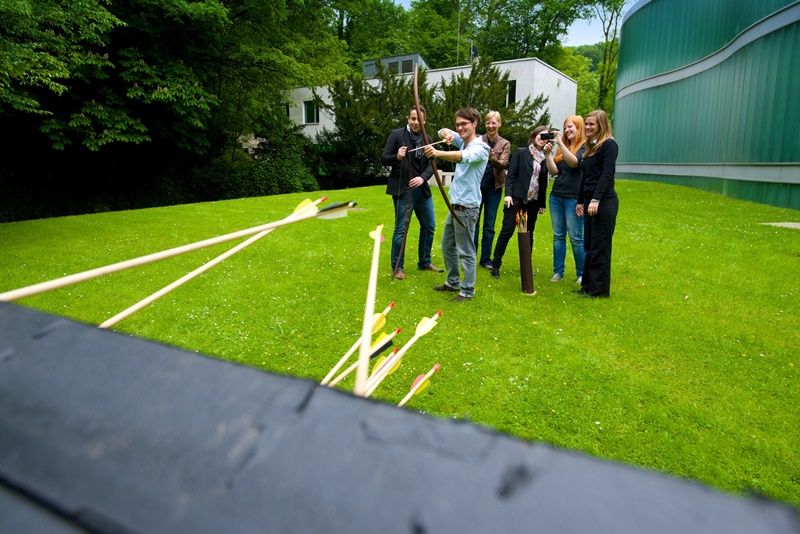 Gruppe von Menschen beim Bogenschießen auf einer Wiese.