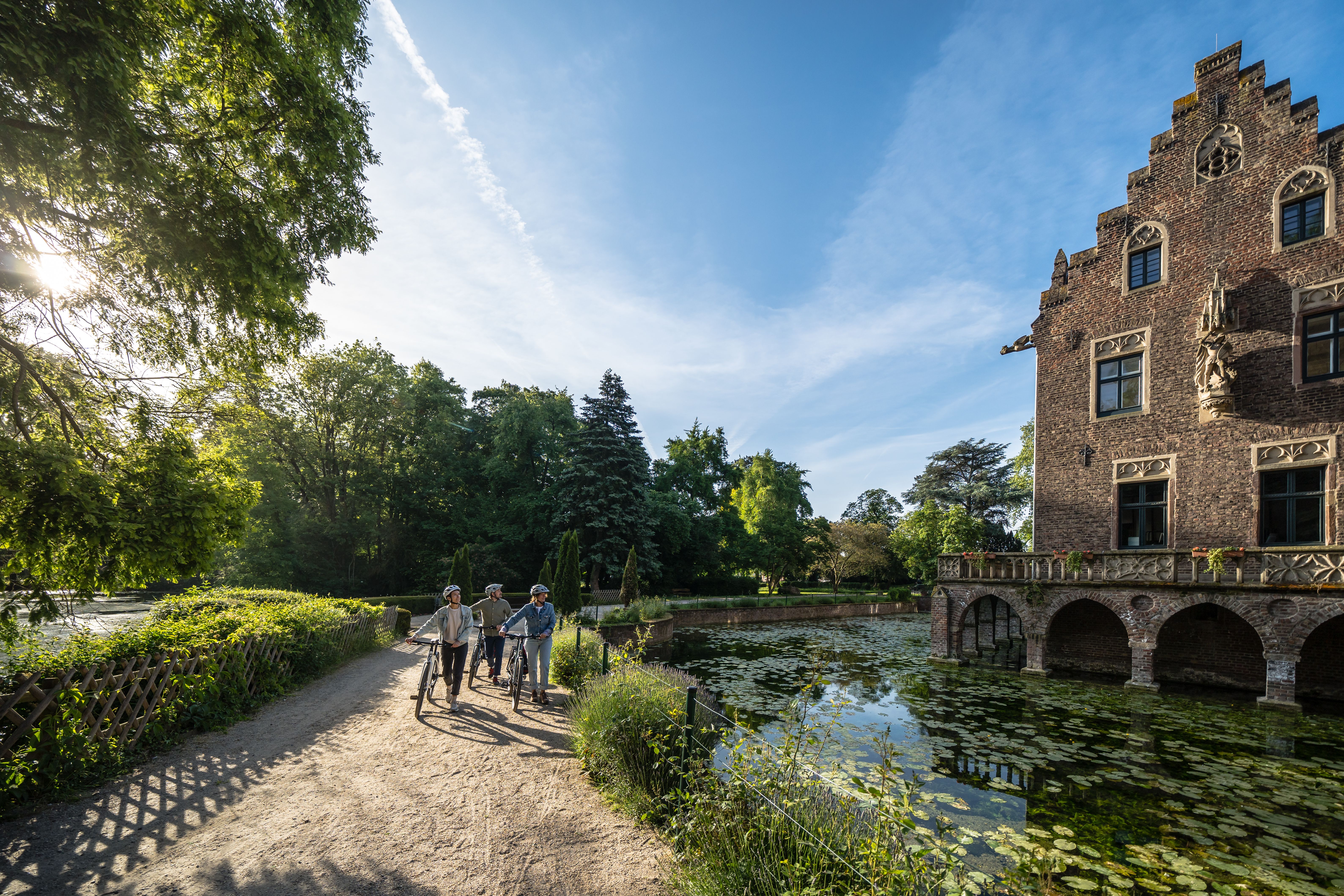 Radfahrer schieben ihre Fahrräder am Schloss Paffendorf in Bergheim entlang.