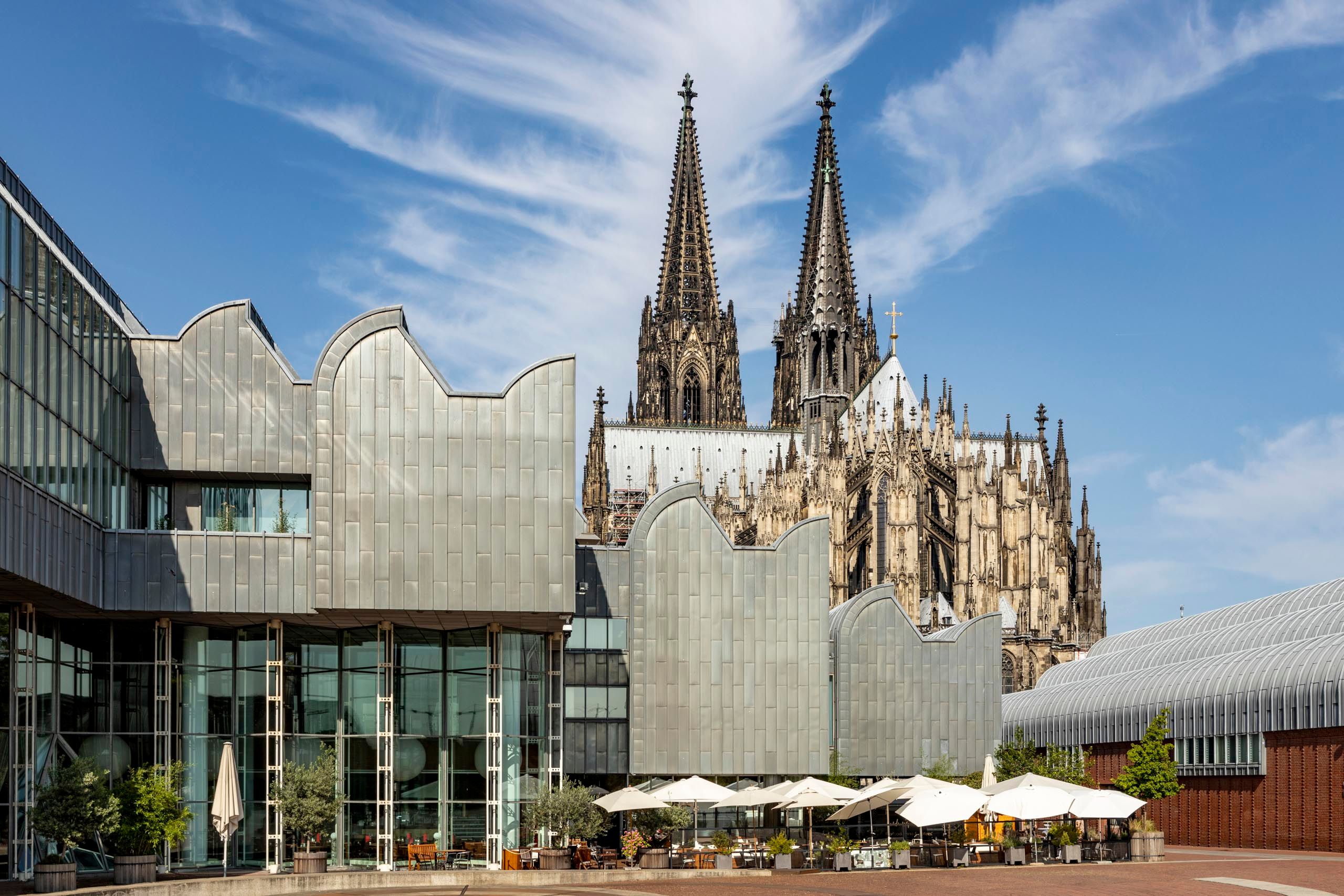 Das Museum Ludwig in Köln mit seiner modernen Architektur, im Hintergrund der imposante Kölner Dom unter blauem Himmel.
