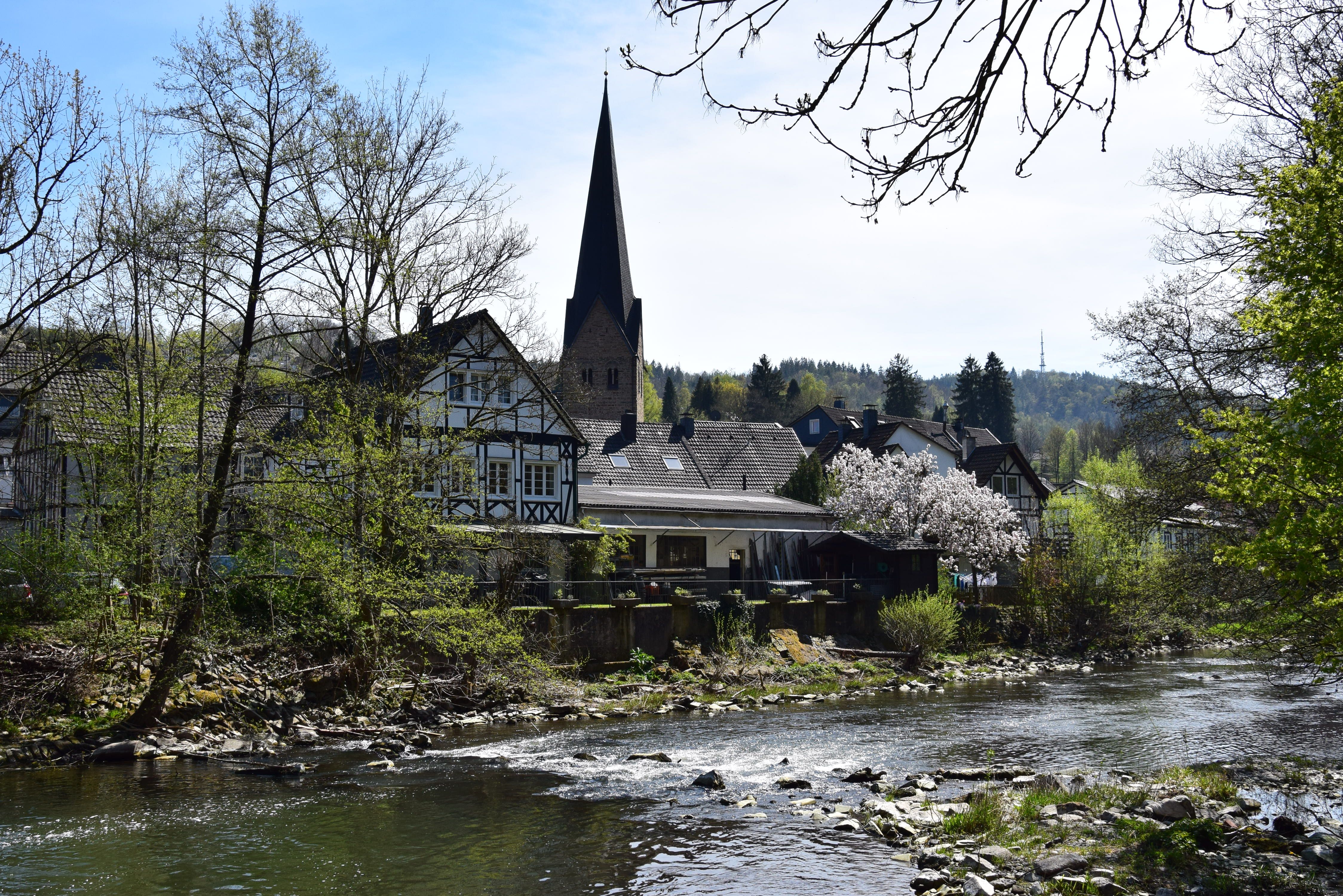 Fluss Agger in Ründeroth mit Fachwerkhäusern und Kirchturm im Hintergrund.