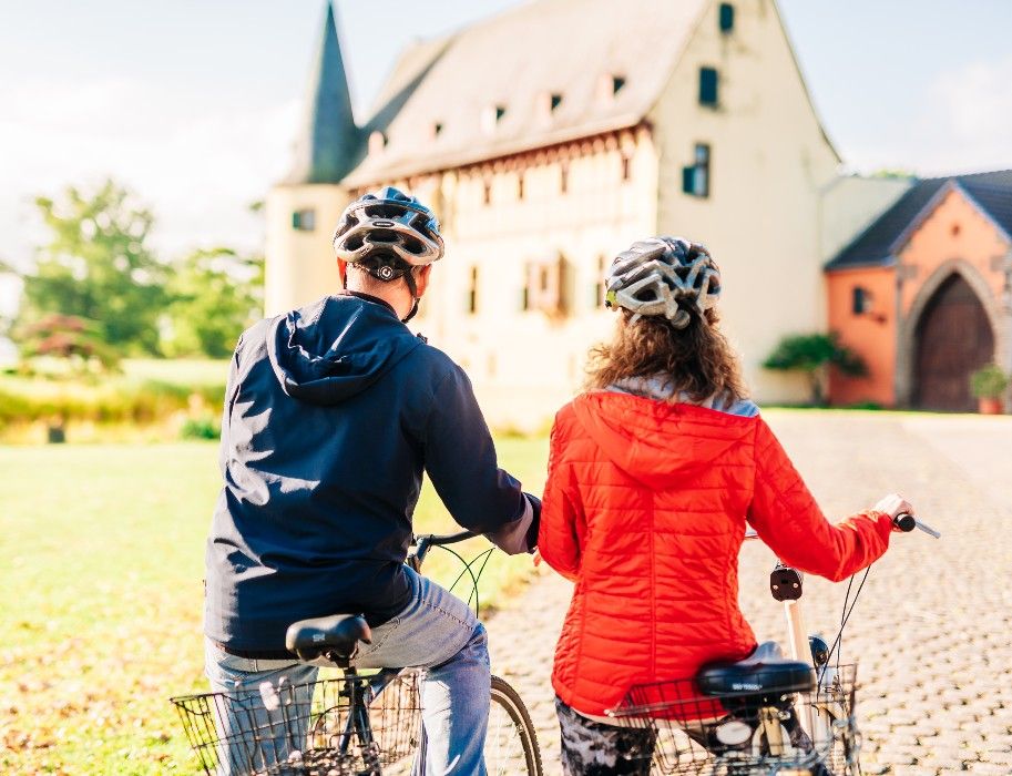 Zwei Radfahrer betrachten die Burg Langendorf in der Nordeifel bei sonnigem Wetter.
