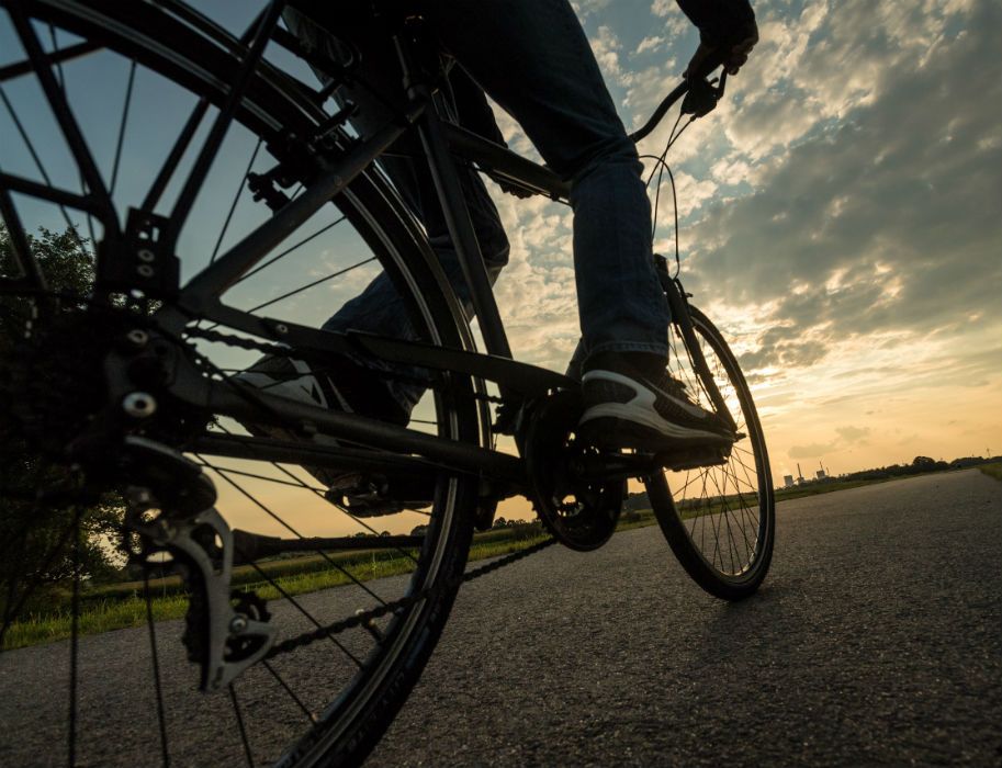 Nahaufnahme eines Fahrrads auf dem Rheinradweg bei Sonnenuntergang. Der Himmel ist teils bewölkt, die Straße führt in die Ferne.