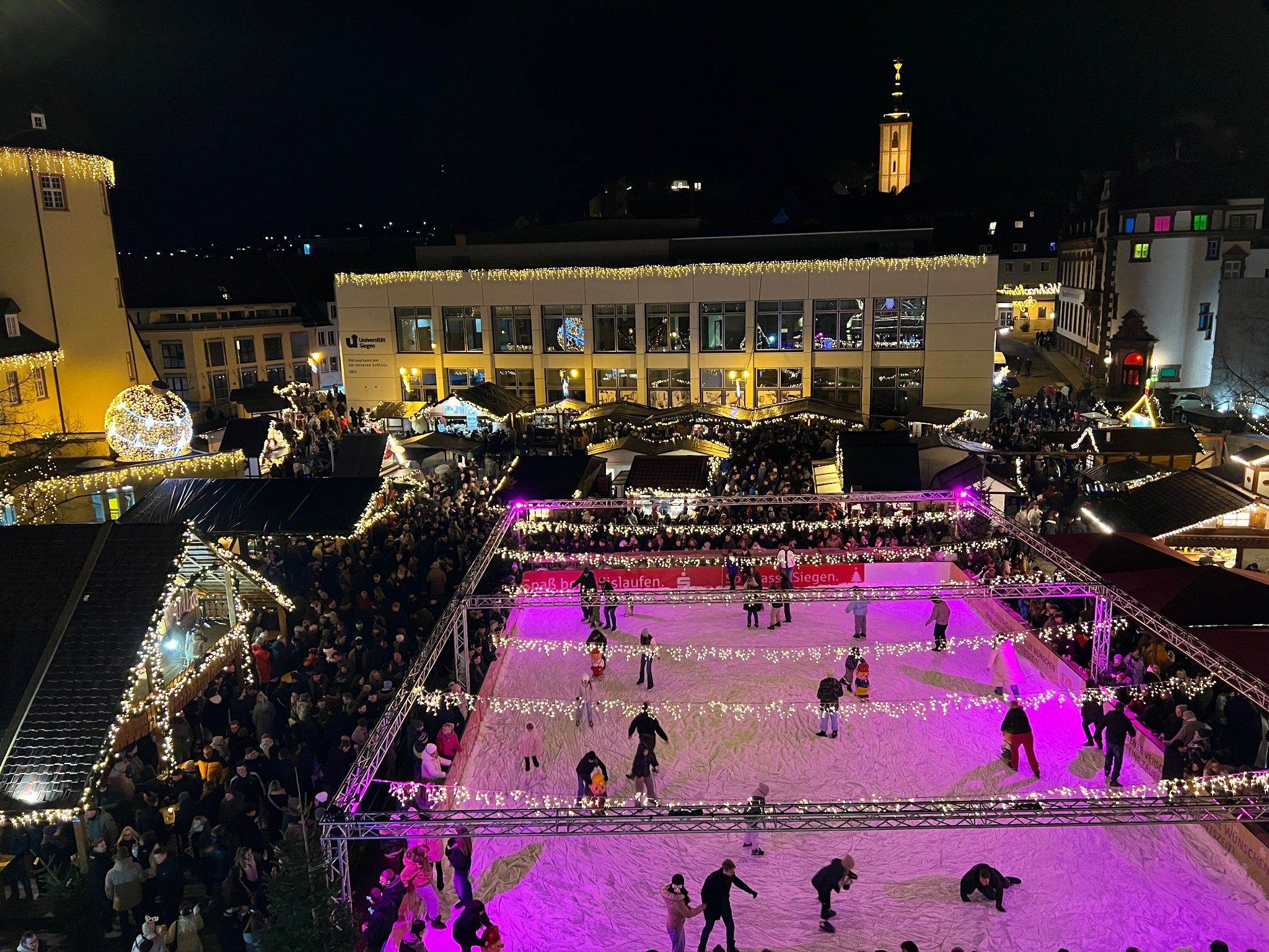 Der Siegener Weihnachtsmarkt am Unteren Schloss zeigt eine beleuchtete Eislaufbahn und festlich geschmückte Stände bei Nacht.