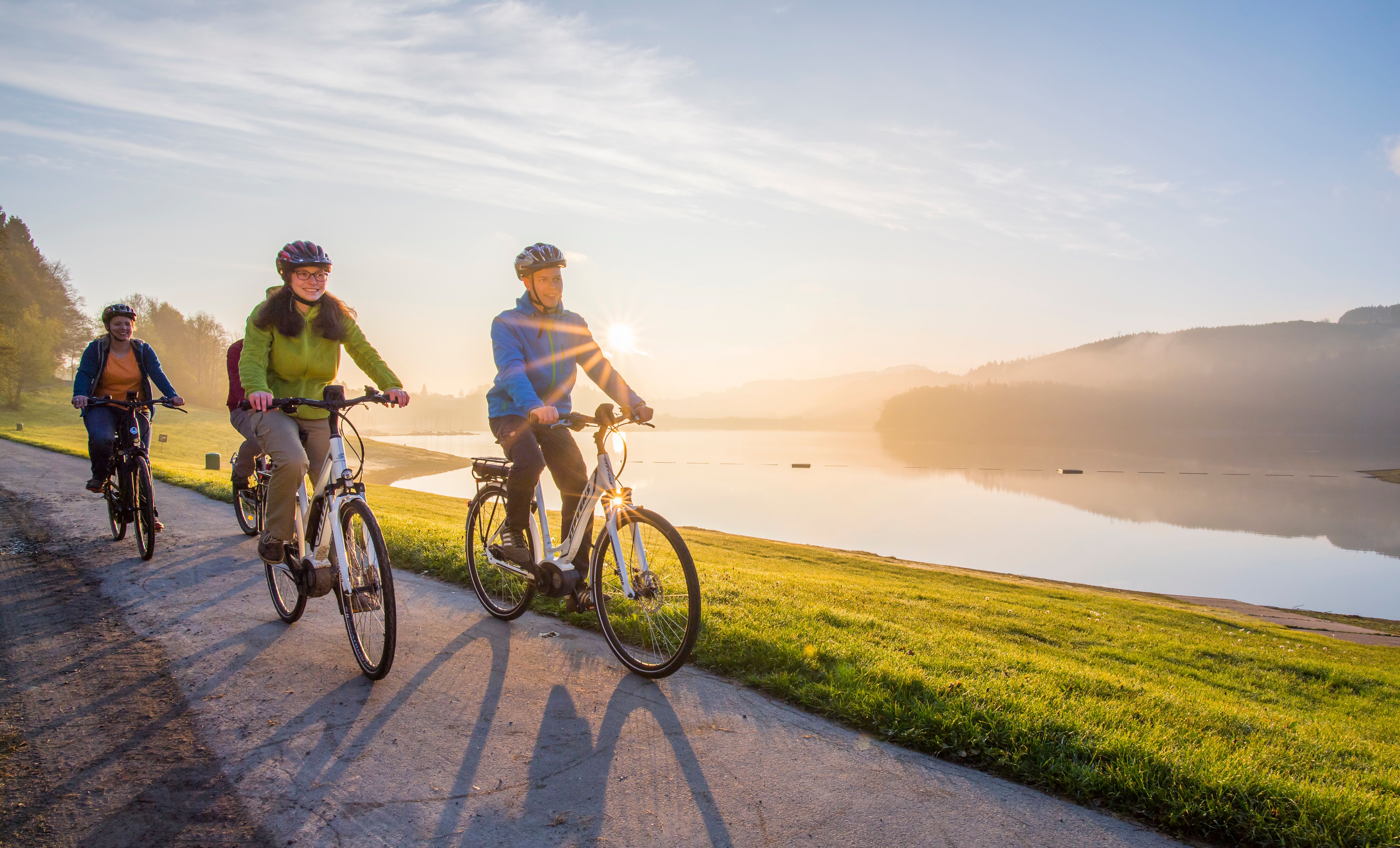 Eine gruppe Radfahrer fährt entlang des Ufers am Hennesee bei mystischer Stimmung am Morgen.