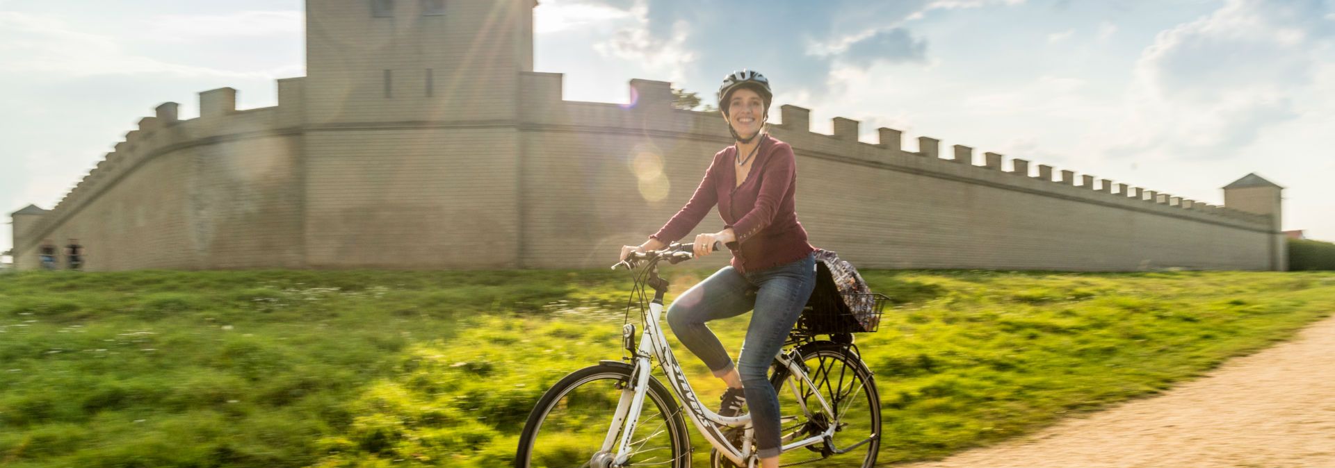 Eine Fahrradfahrerin fährt bei Sonnenschein vor der Via Romana entlang.