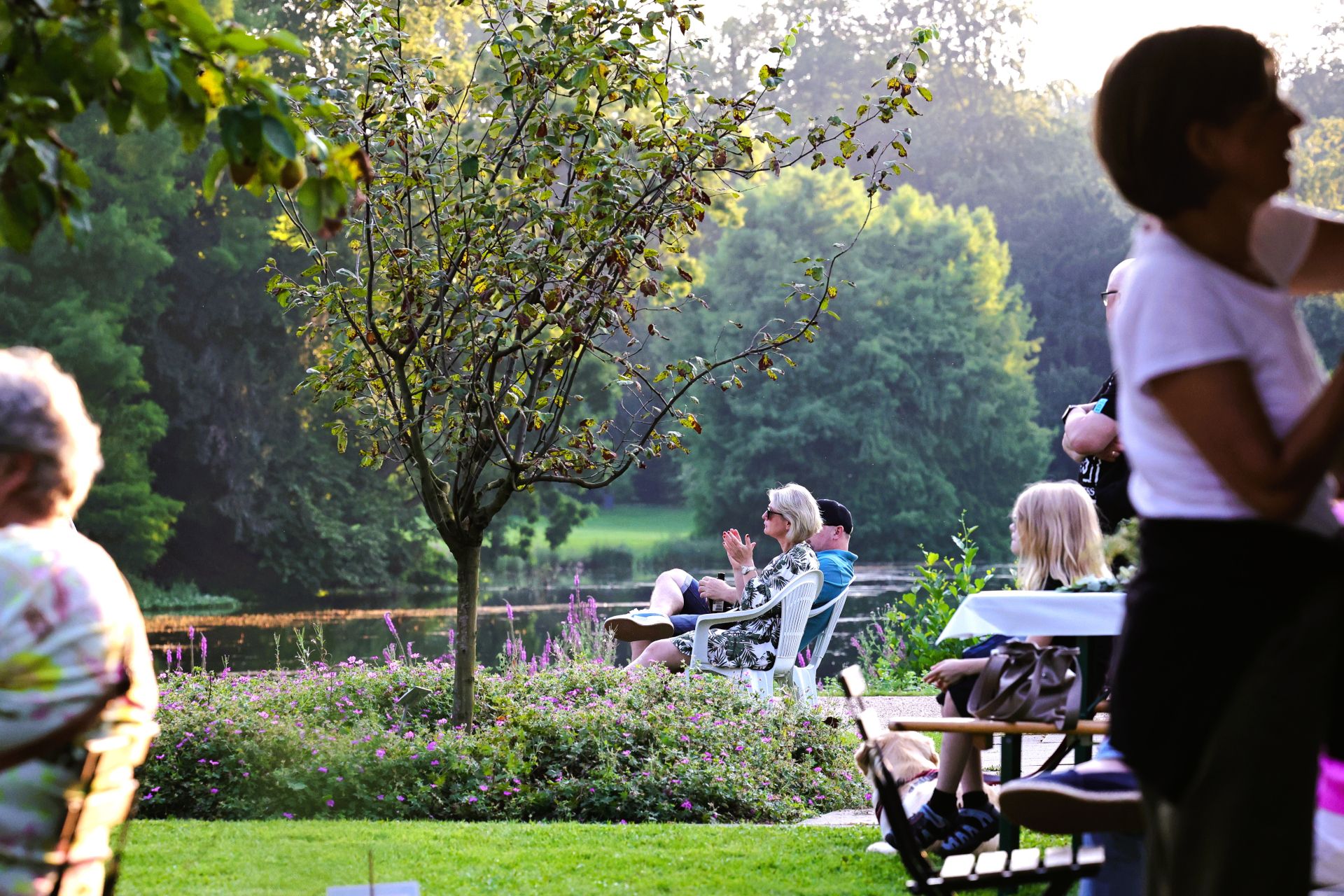 Besuchende entspannen im Schlosspark von Schloss Dyck, umgeben von grüner Natur und einem kleinen Teich. Die Stimmung beim SchlossSommer ist friedlich und einladend