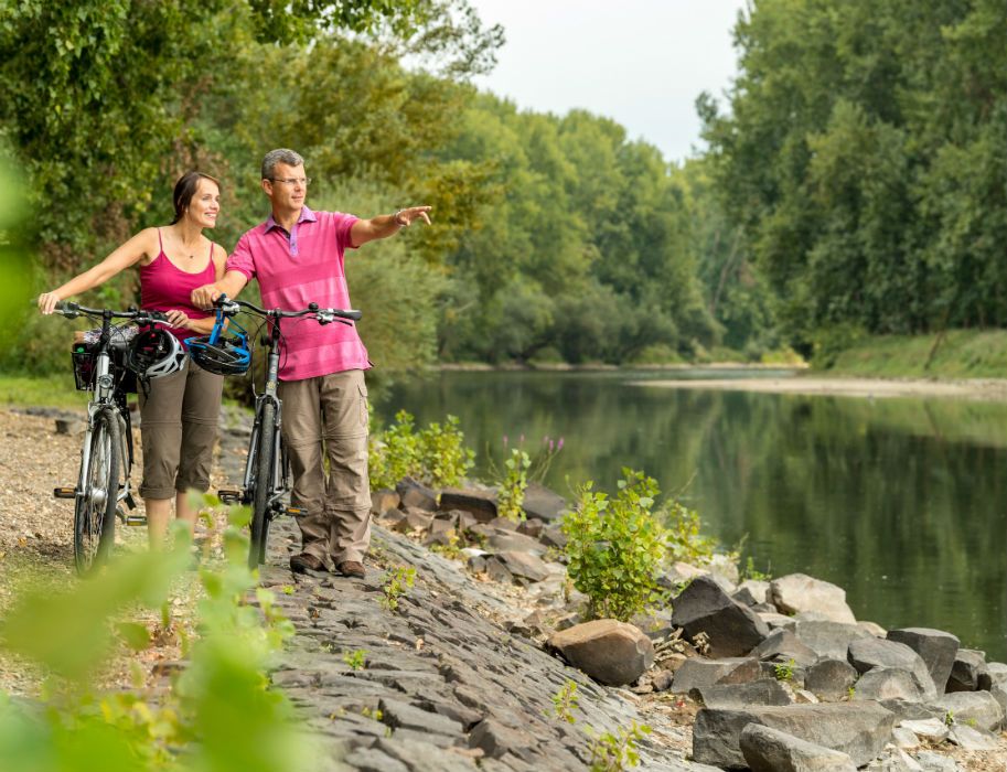 Zwei Personen stehen mit Fahrrädern am Ufer des Niers, umgeben von Bäumen.
