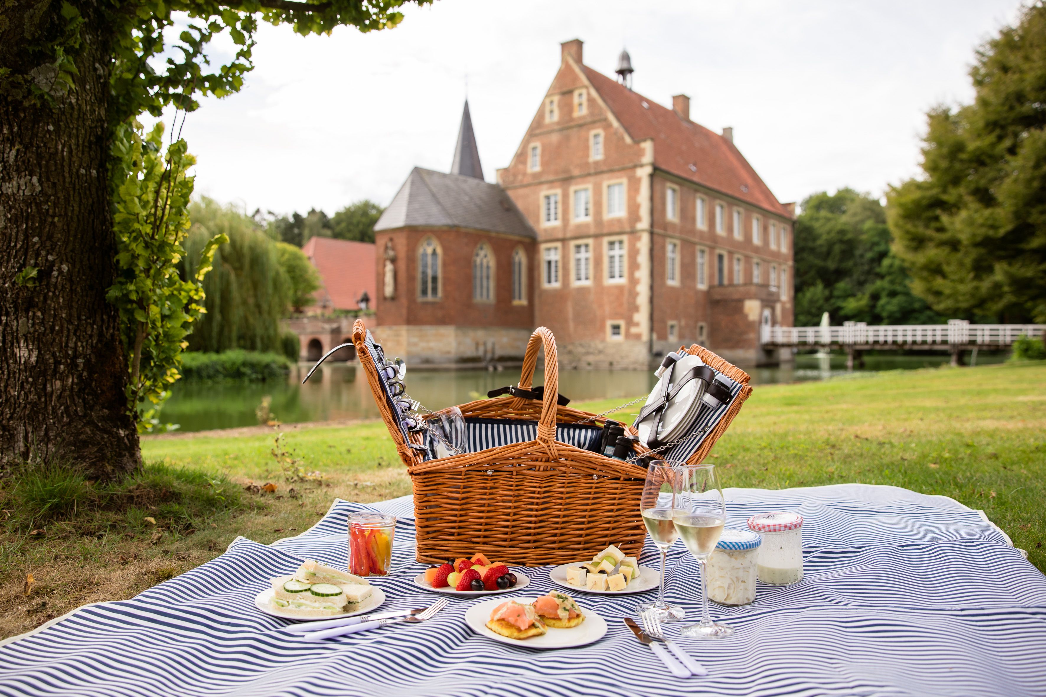 Ein Picknick-Korb auf einer Decke vor der Burg Hülshoff mit Speisen und Getränken.