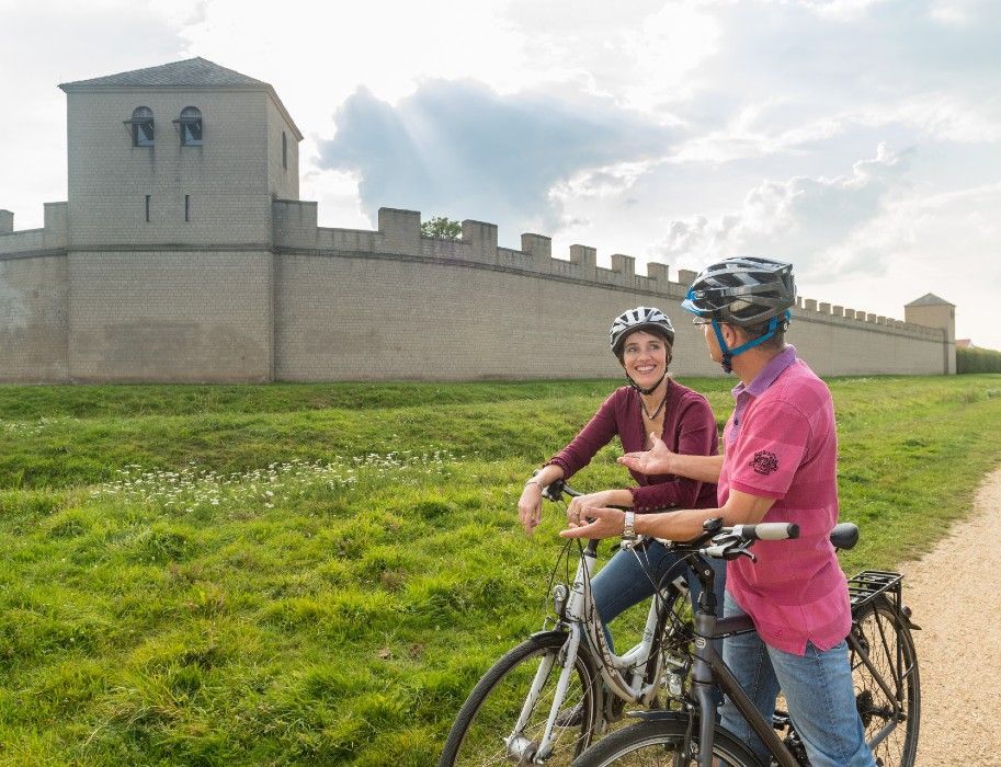 Zwei Radfahrer tauschen sich vor einer historischen Mauer am Archäologischen Park Xanten über ihre Erlebnisse aus