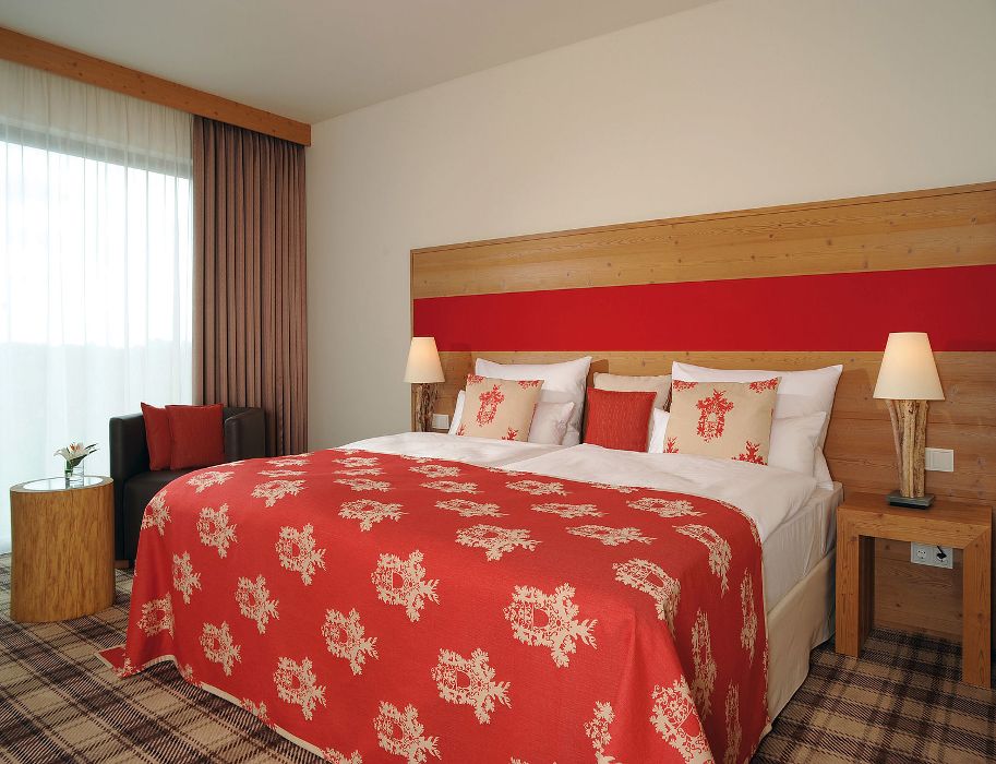 Hotelzimmer mit großem Bett, roter Bettdecke und Holzelementen.