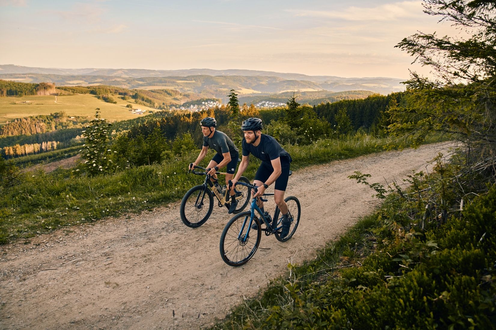 Zwei Gravelbiker fahren auf Schotterweg, dahinter weiter Landschaftsblick