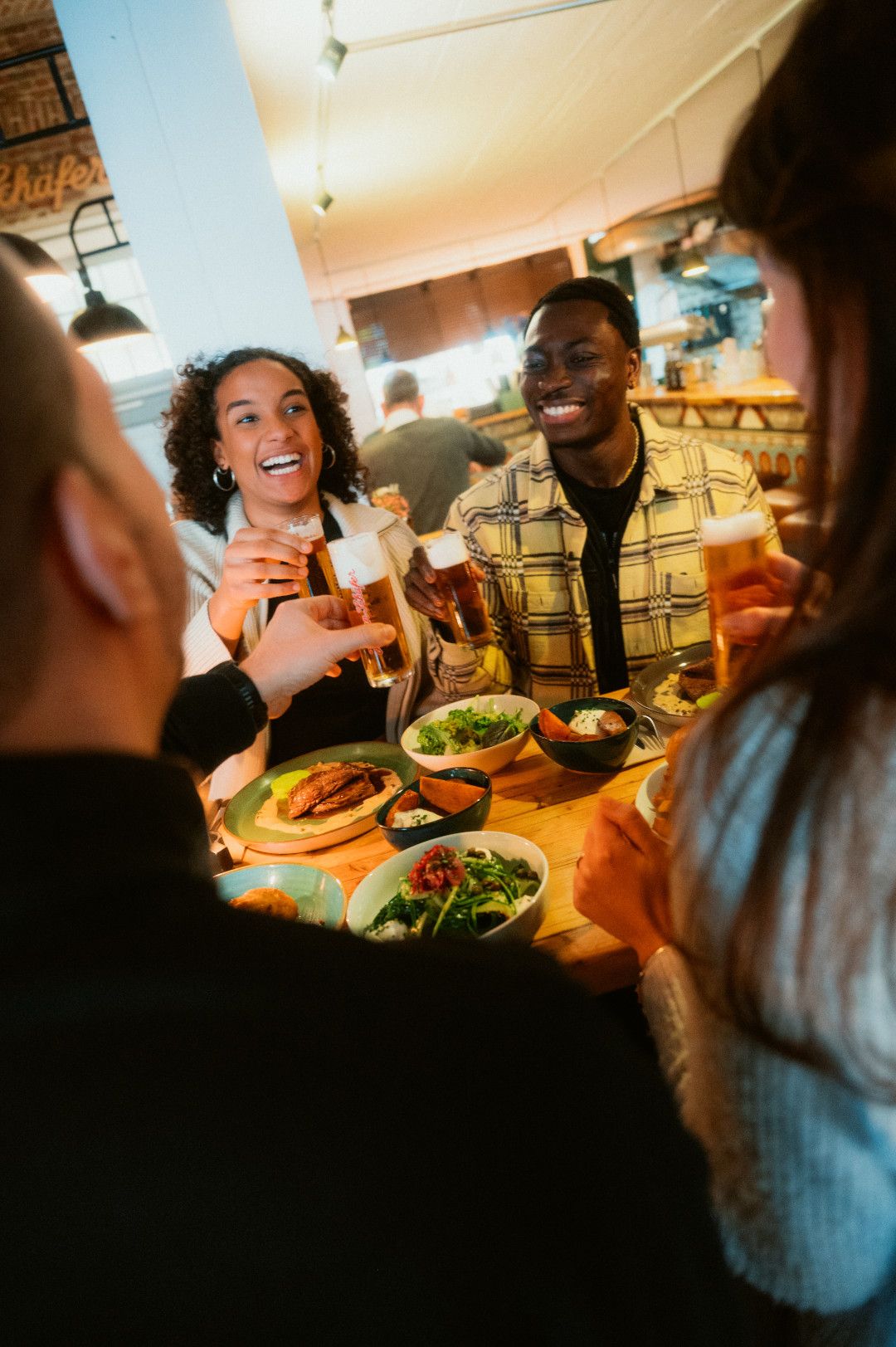 Vier Menschen stoßen an mit Kölsch, auf dem Tisch steht Essen