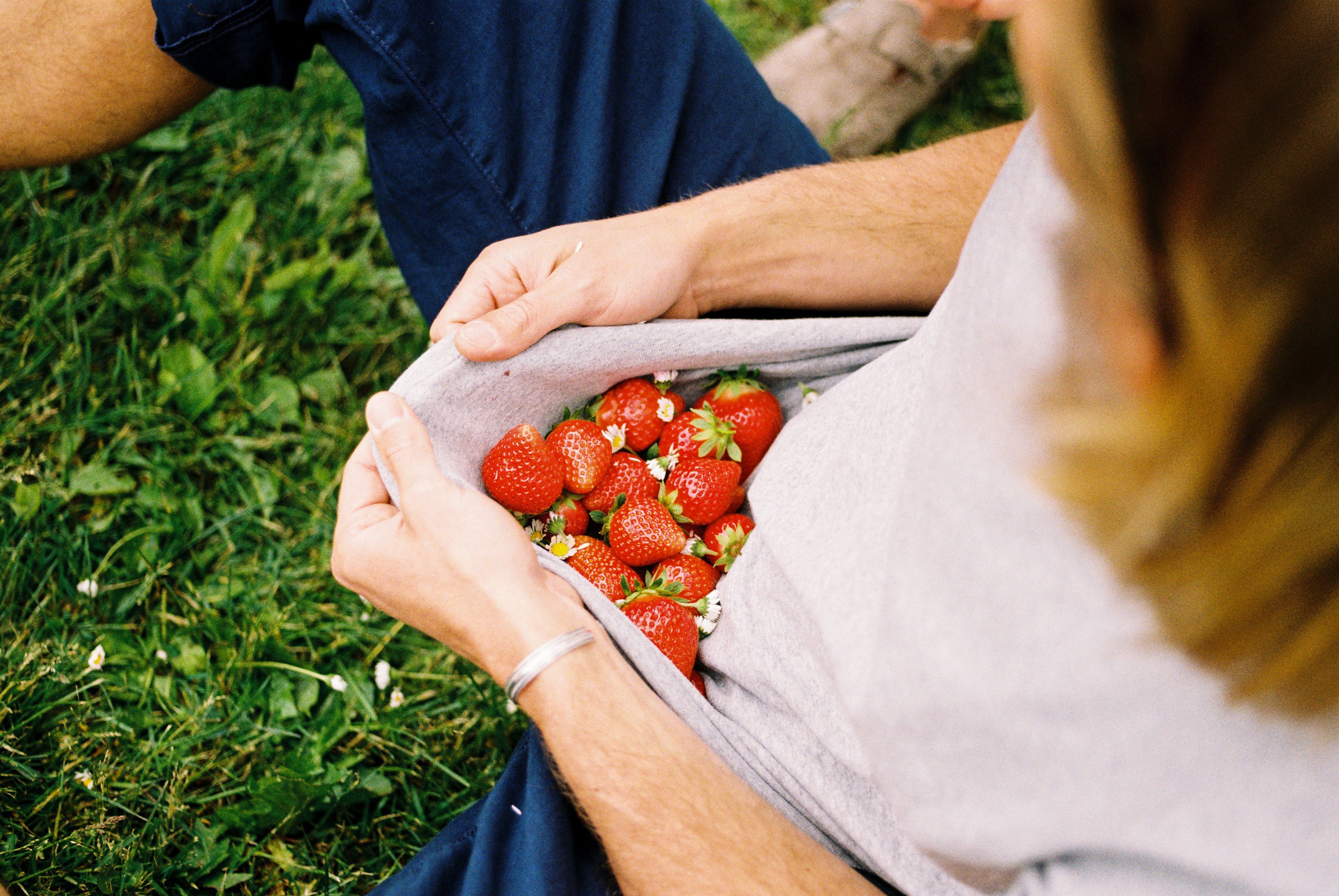 Frau hält mehrere Erdbeeren in ihrem Shirt auf dem Obstgut Mönchshof im Bergischen Land.