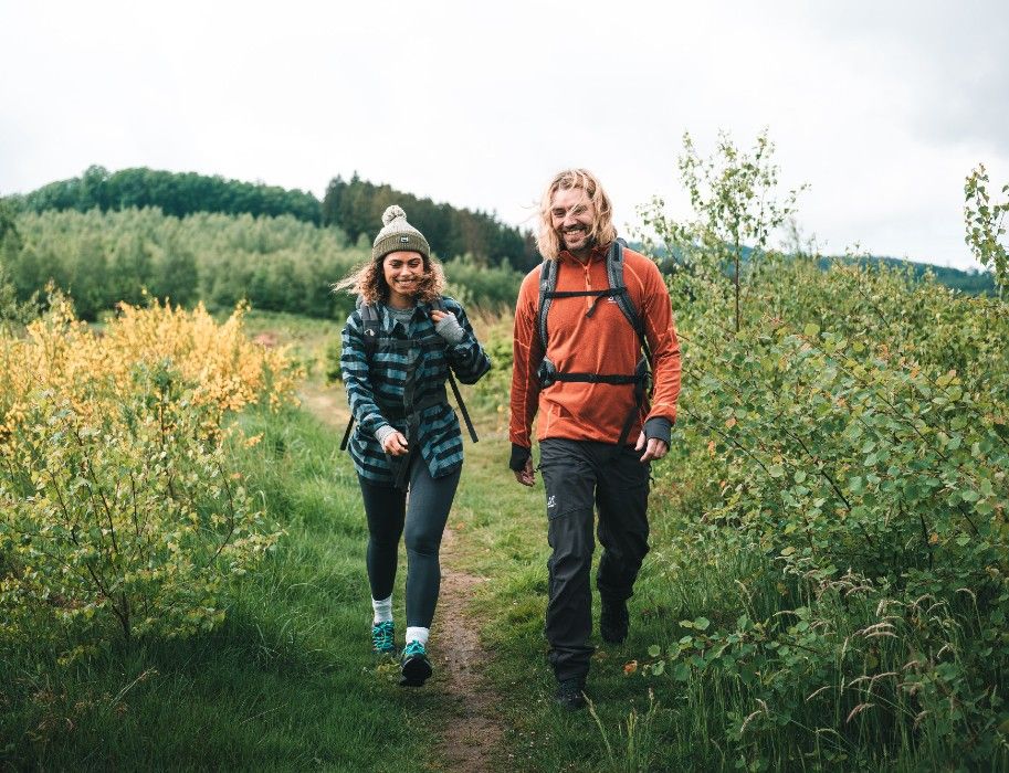 Zwei Wanderer auf einem Pfad im Grünen, umgeben von Büschen und Bäumen.