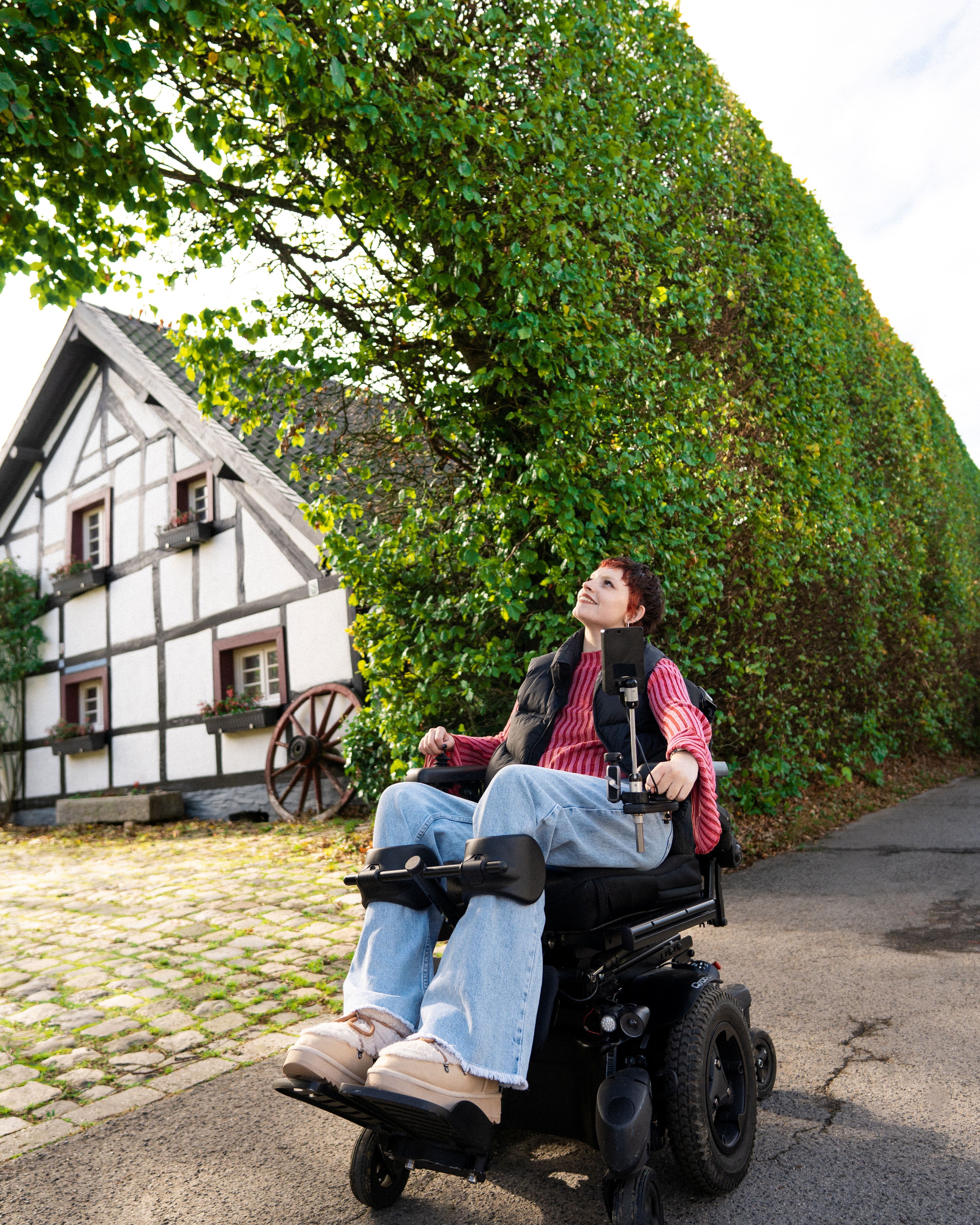 Eine Rollstuhlfahrerin genießt den Anblick der Haushecke und des Fachwerkhauses in Monschau-Höfen