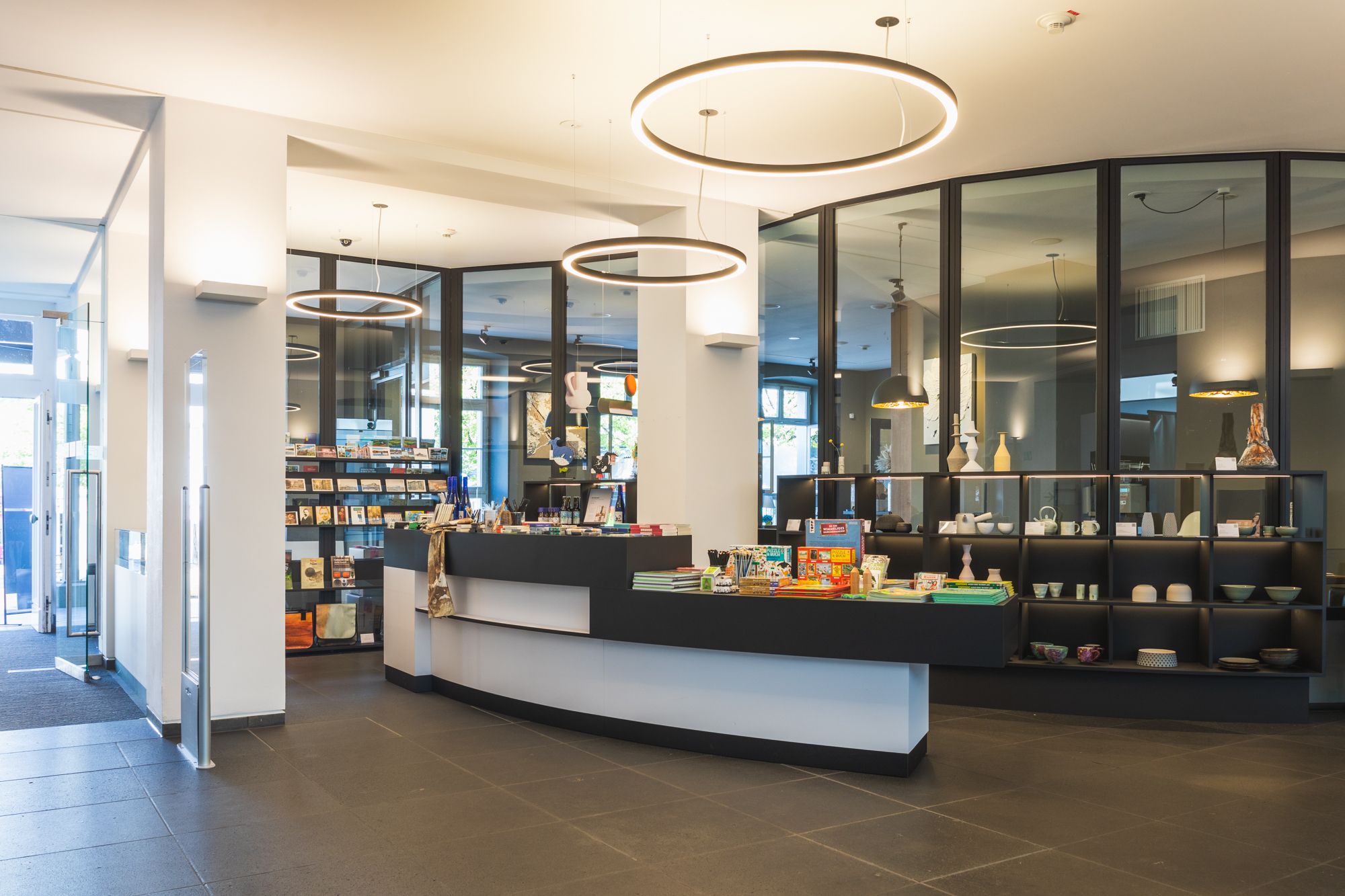Moderner Museumsshop mit schwarzen Regalen, runden Deckenleuchten und Souvenirs auf der Theke.
