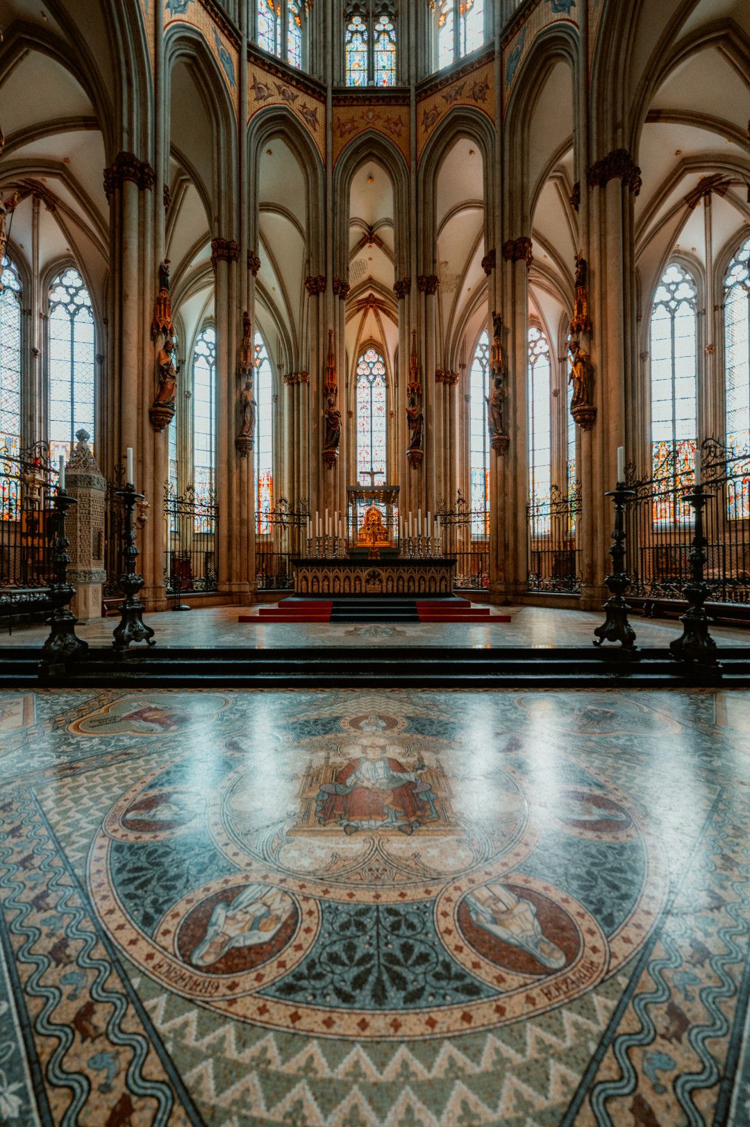 Der Innenraum des Kölner Doms zeigt ein kunstvolles Mosaik auf dem Boden und hohe gotische Fenster, die den Raum mit Licht durchfluten.