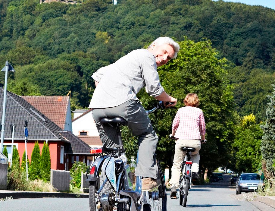 Zwei Personen fahren mit E-Bikes auf einer Straße, umgeben von Häusern und Bäumen. Sie sind auf dem Weg zum Kaiser-Wilhelm Denkmal.