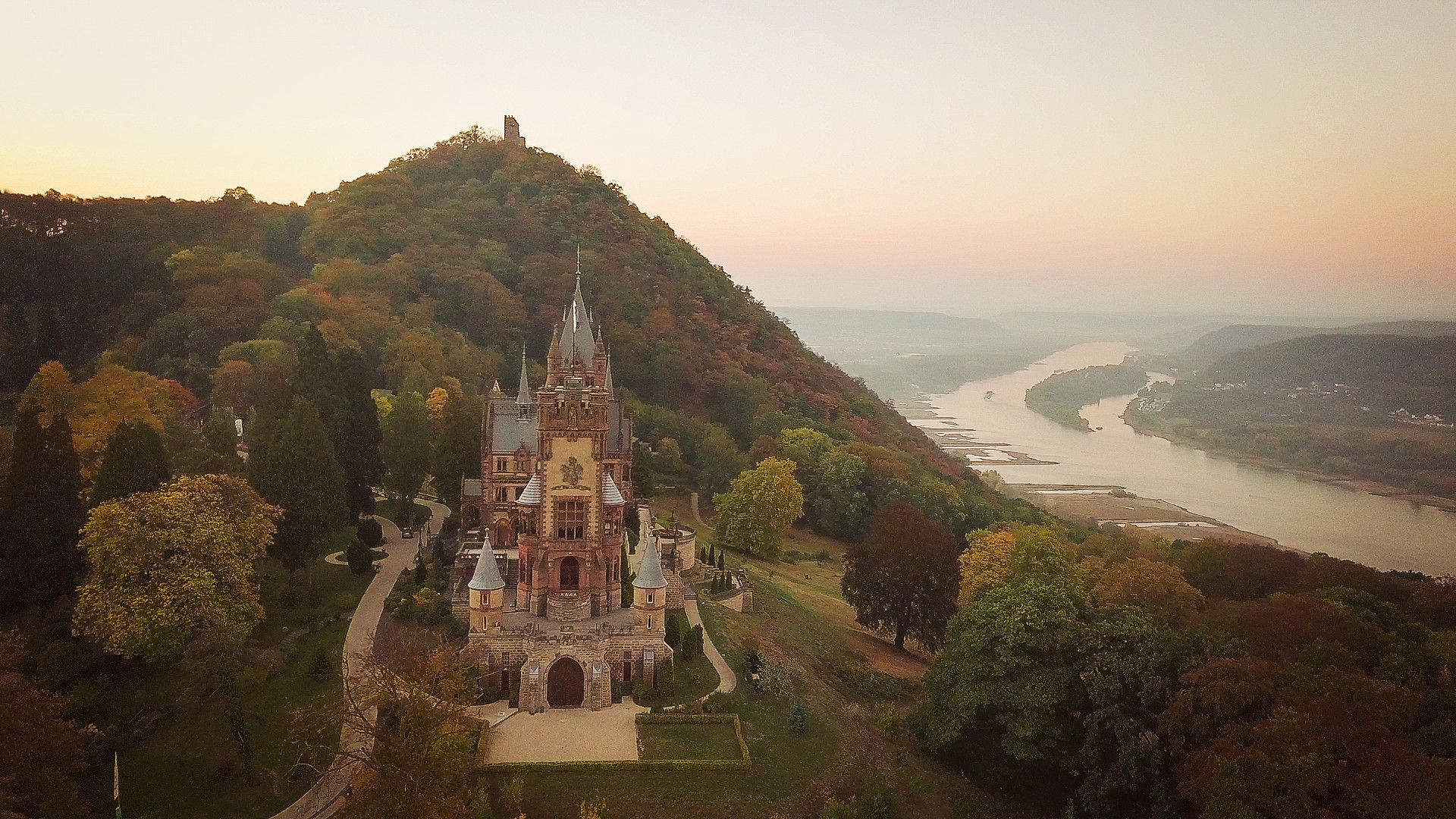 Schloss in bewaldeten Bergen und mit Fluss im Hintergrund