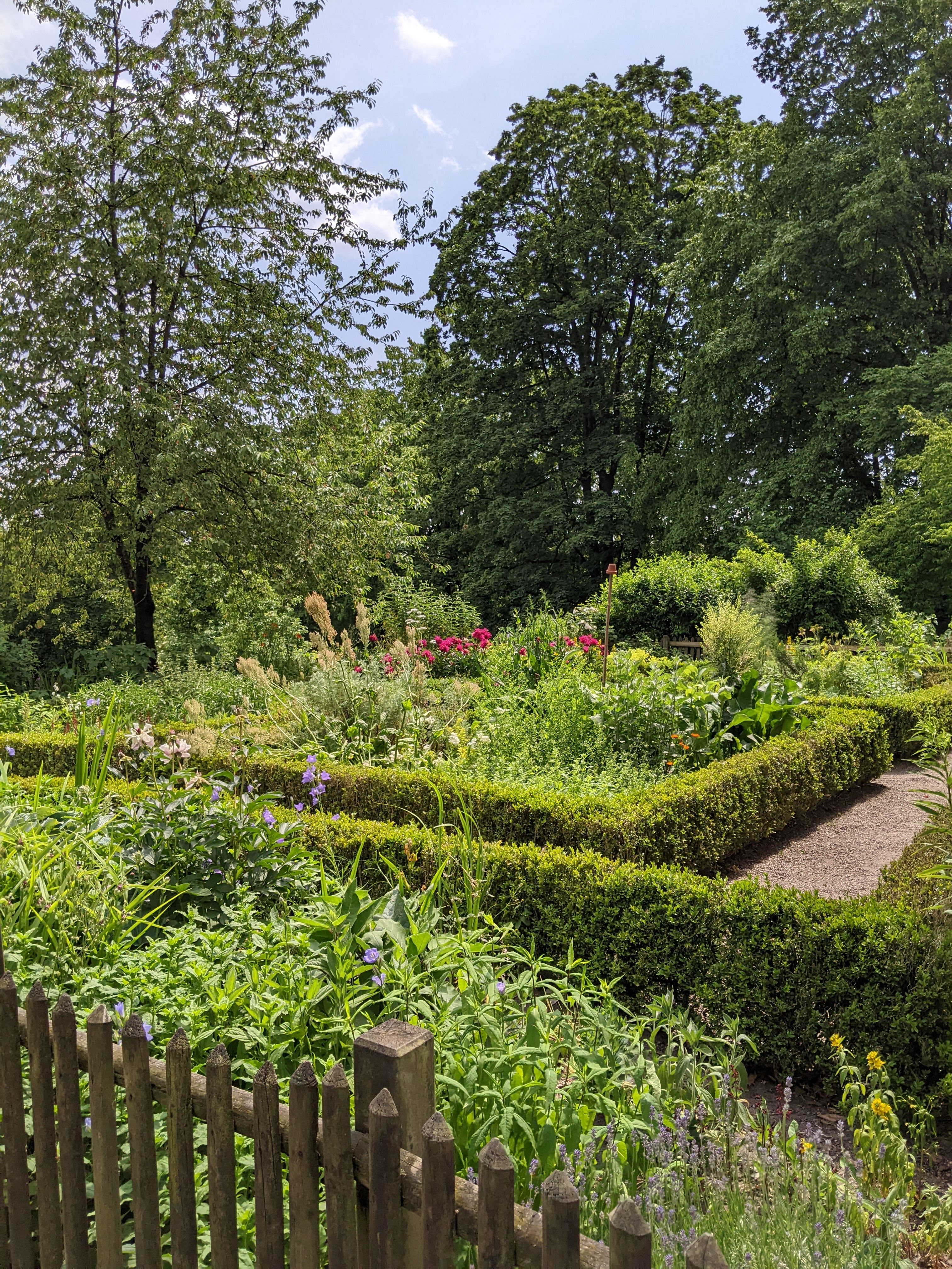 Ein gepflegter Garten im Bauernhausmuseum in Bielefeld mit bunten Blumenbeeten, umgeben von grünen Hecken und hohen Bäumen.